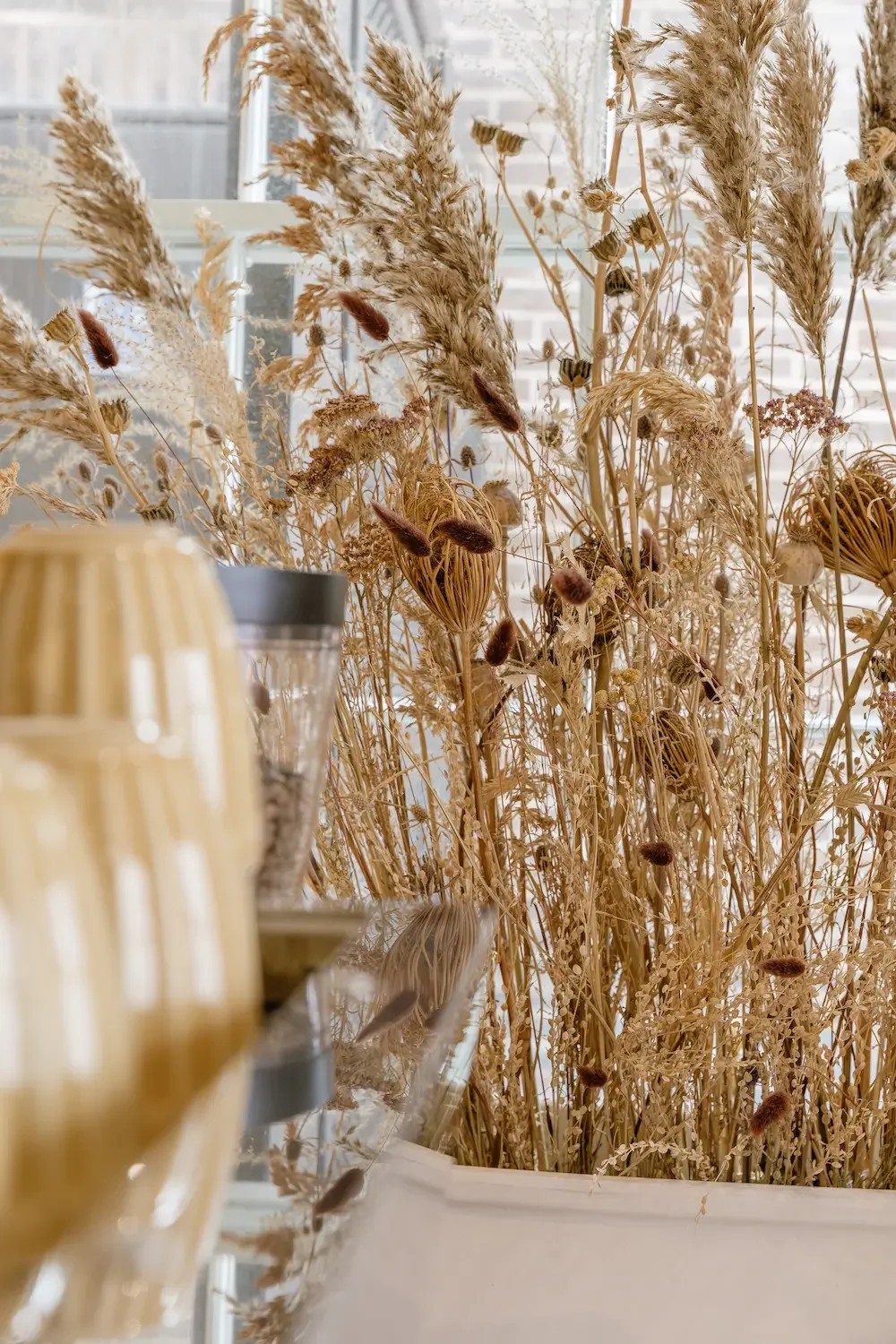 Large dried botanical arrangement in white planter on coffee shop windowsill
