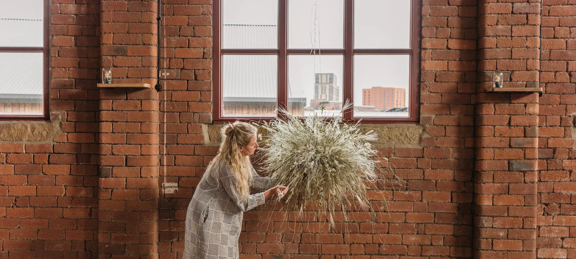 Jess at Anther creating a suspended wall hanging made of dried grasses and flowers
