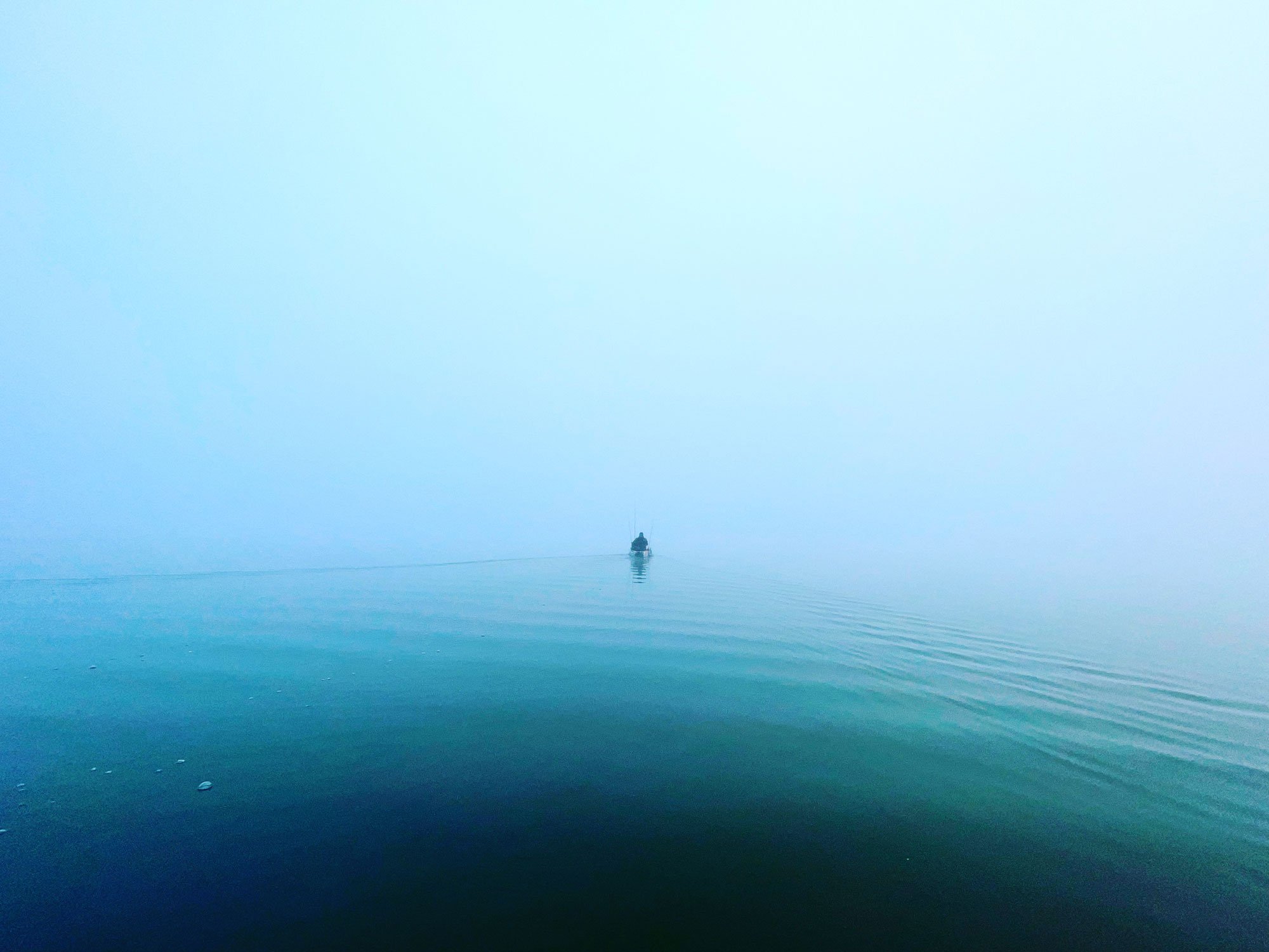 Un paysage brumeux avec un lac calme et un petit bateau au loin.