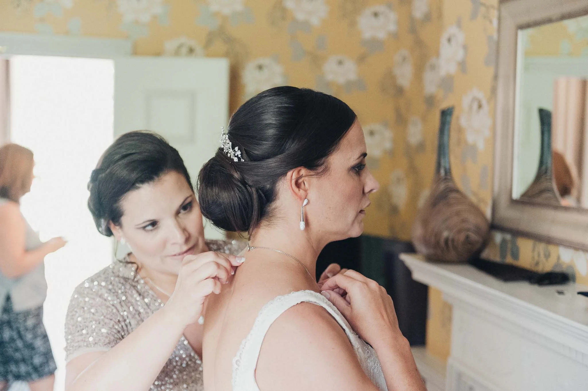 Bridesmaid fastening the bride’s necklace during morning preparations.