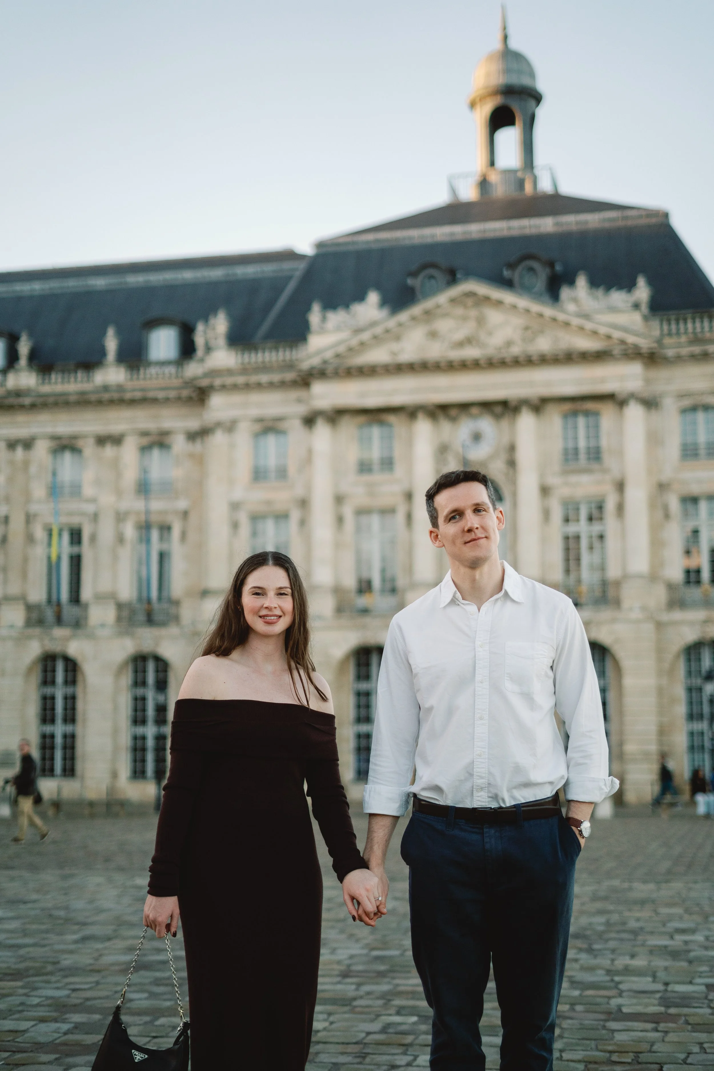 Engaged couple holding hands in Place de la Bourse during an engagement session in Bordeaux.