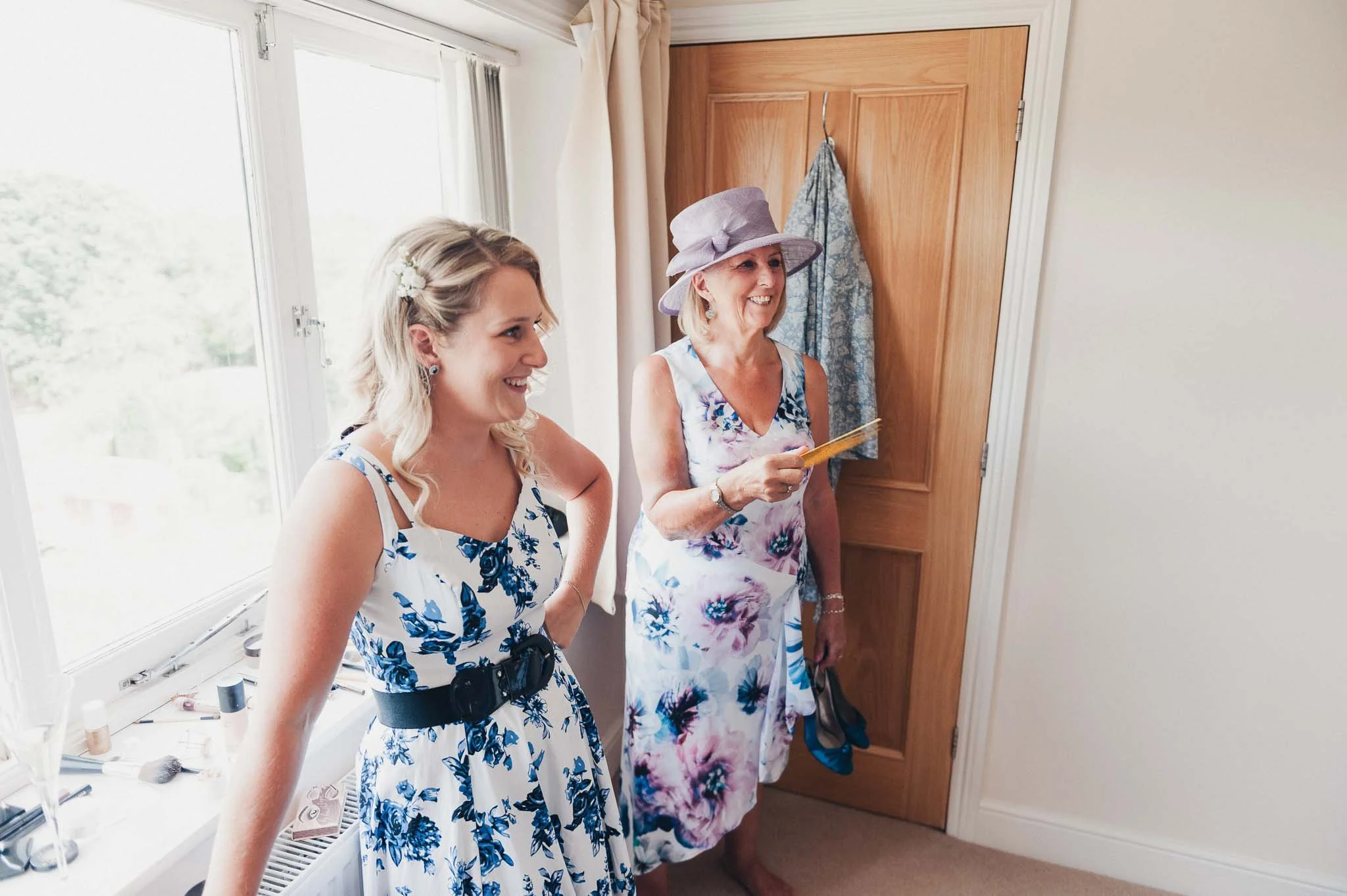 Bridesmaids standing by the window chatting during bridal prep.