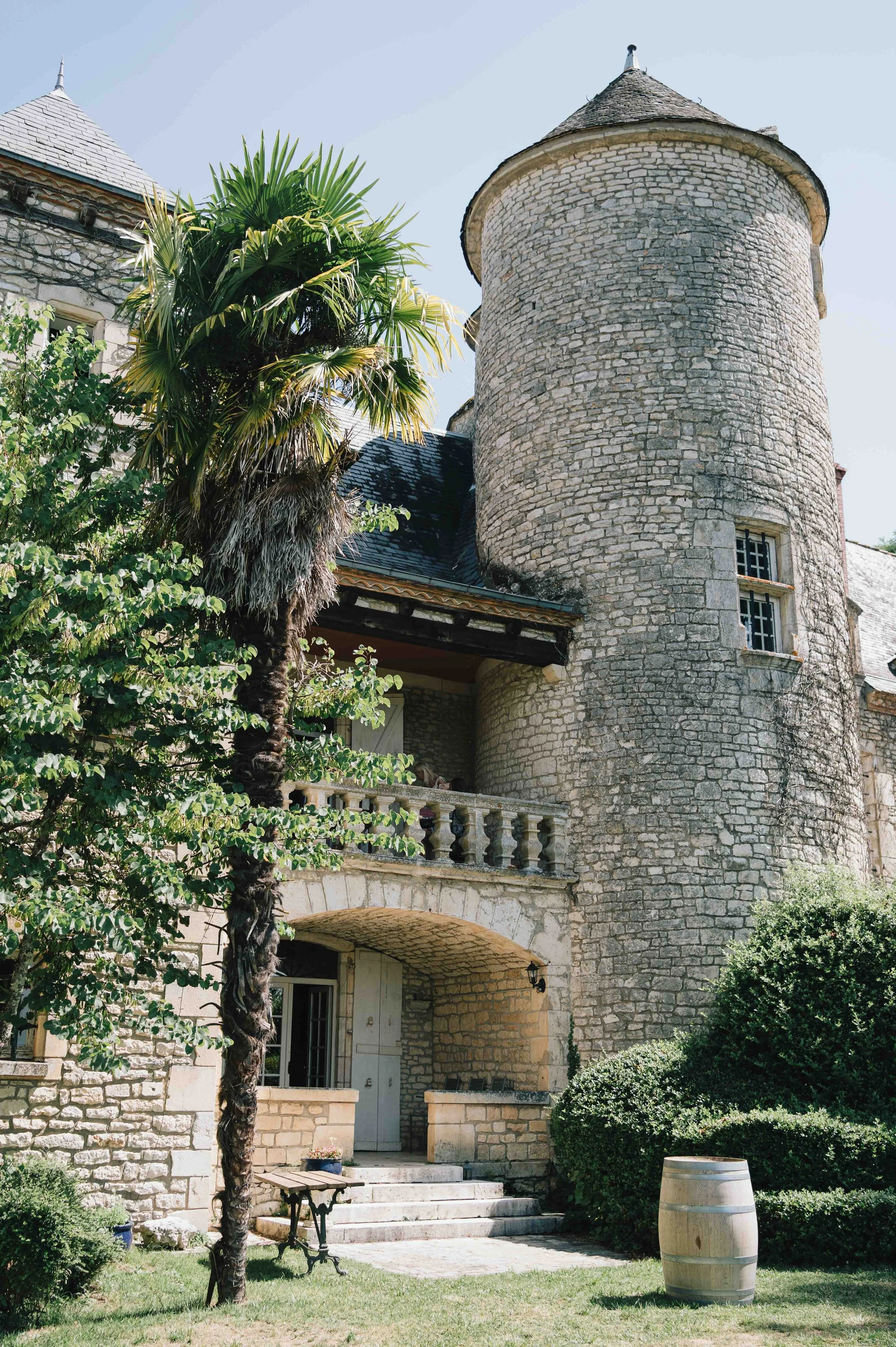 Exterior of Château du Raysse with stone turret, arched doorway, and palm tree in the foreground