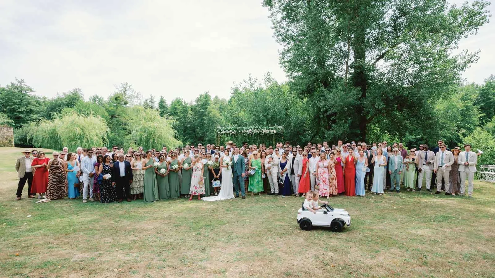 Full group photograph of the wedding guests on the lawn at Château Lagorce, with the remote control car in front