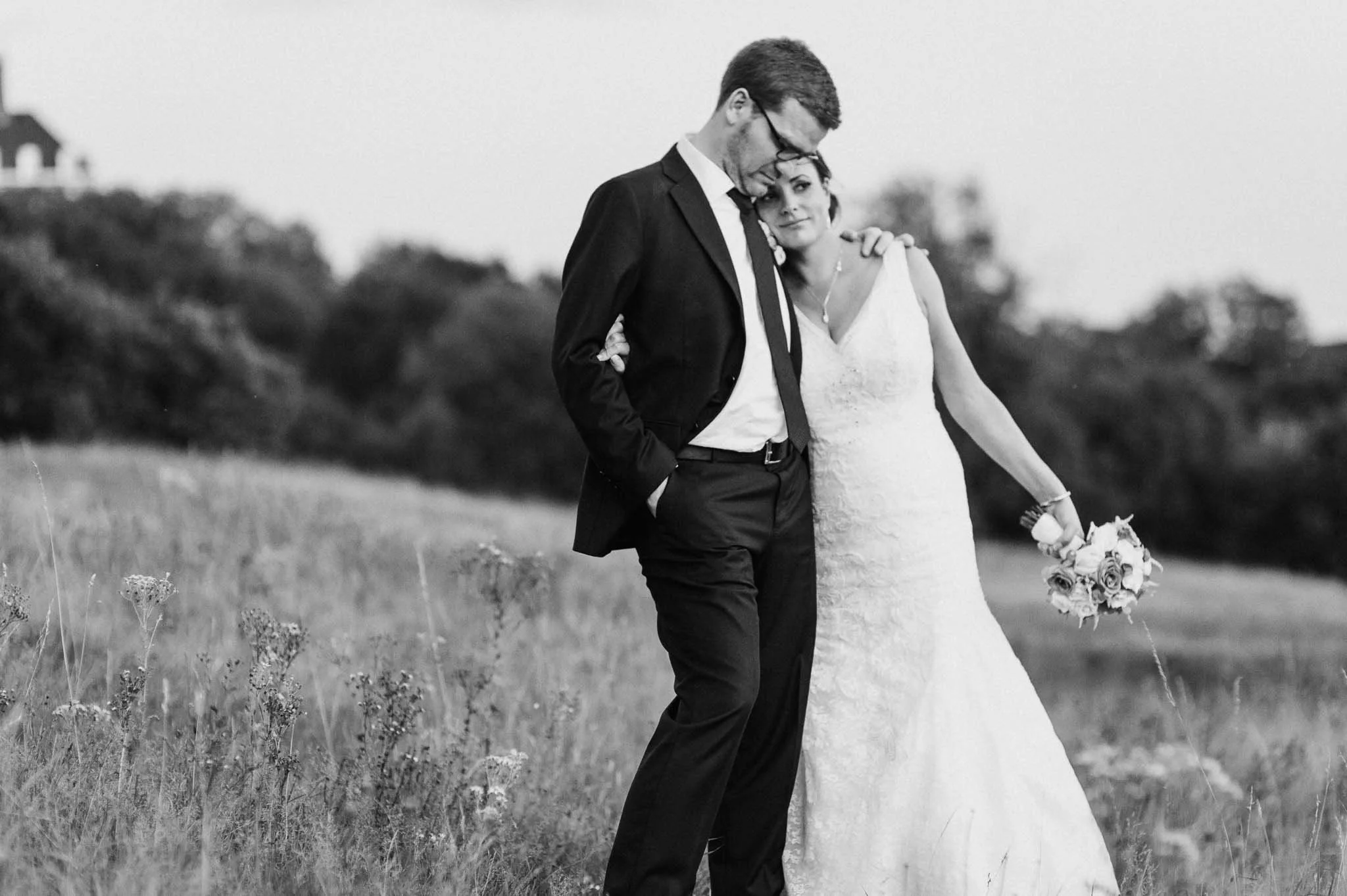 Black-and-white photo of the couple walking across a field, laughing together.