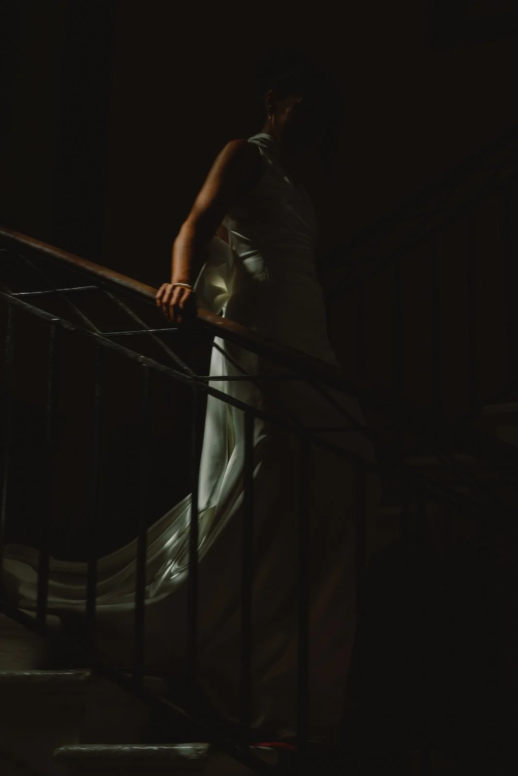 The bride coming down a dark staircase in window light at Château Lagorce