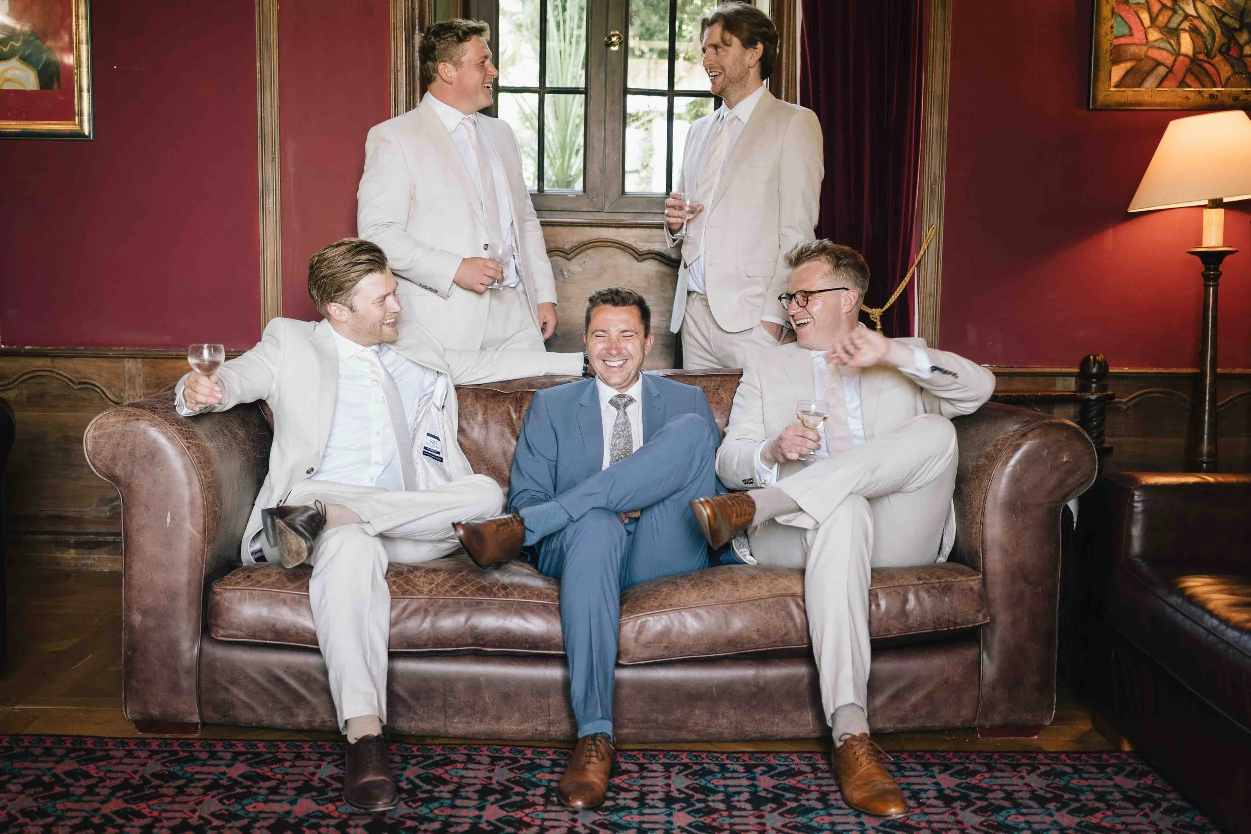 Groom and groomsmen sharing a laugh on a leather sofa before the ceremony at Château du Raysse
