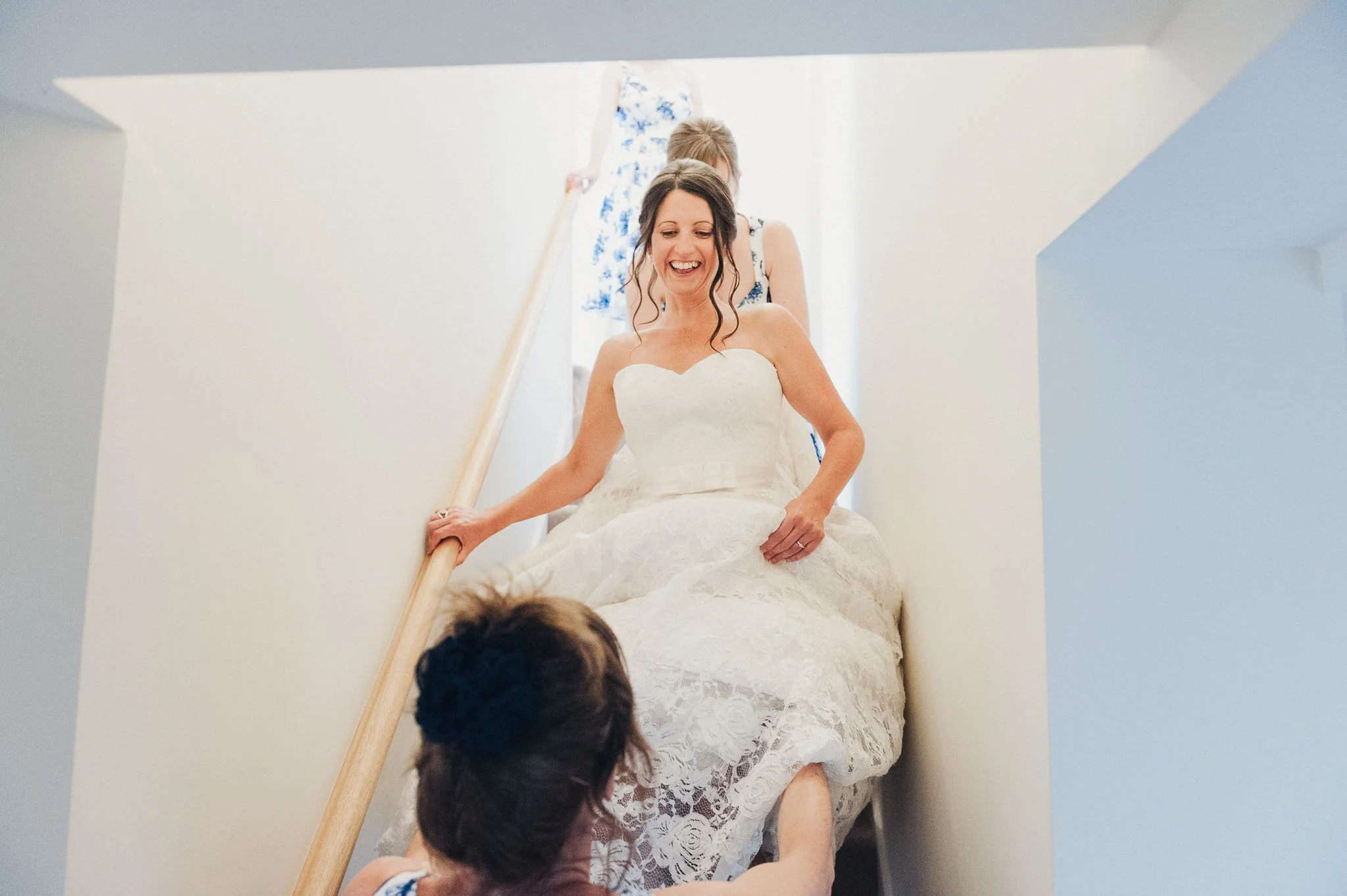 The bride smiling while being guided down a narrow staircase, her dress gathered around her.
