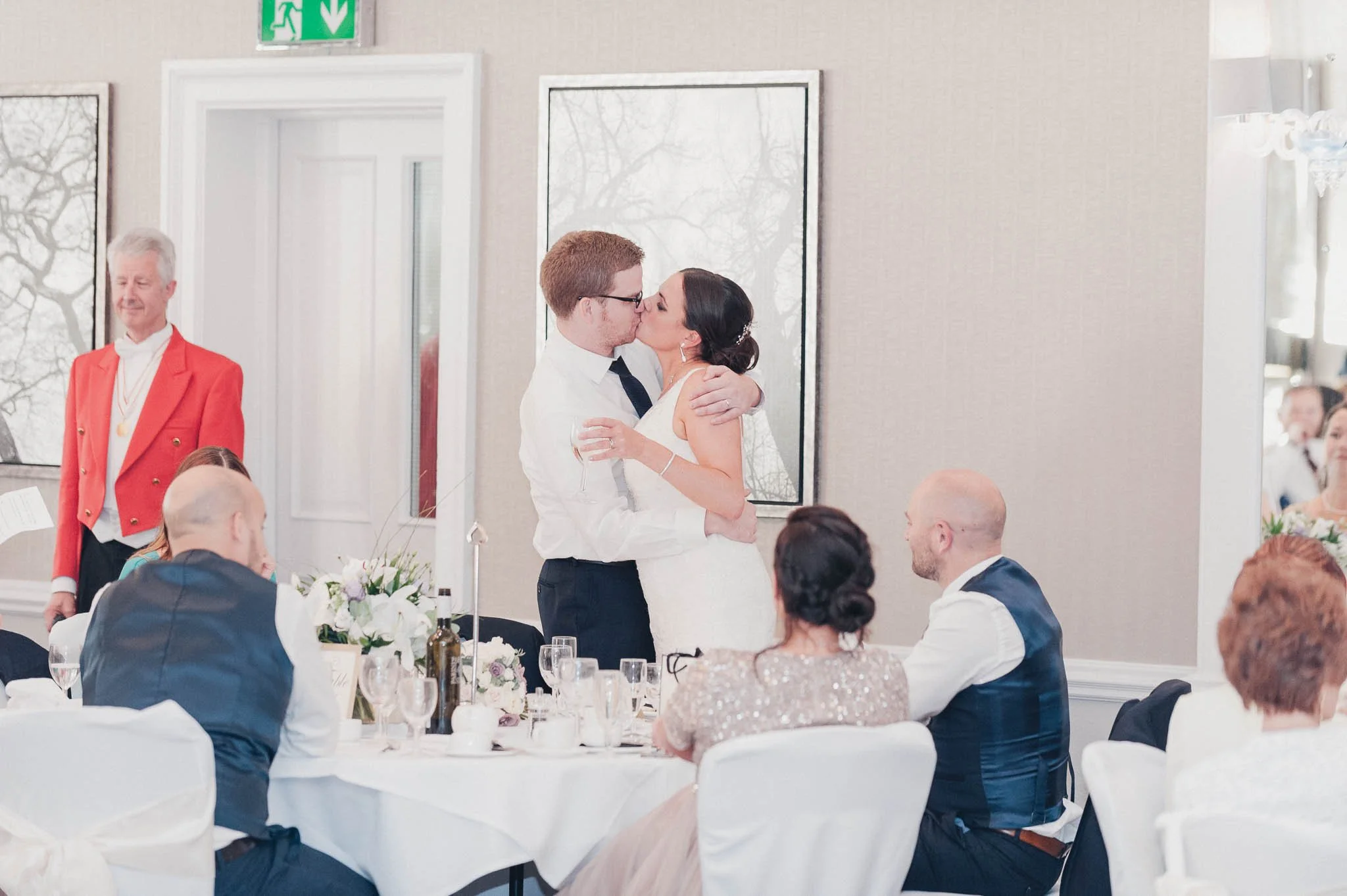 The bride and groom standing to kiss during the speeches as guests applaud.
