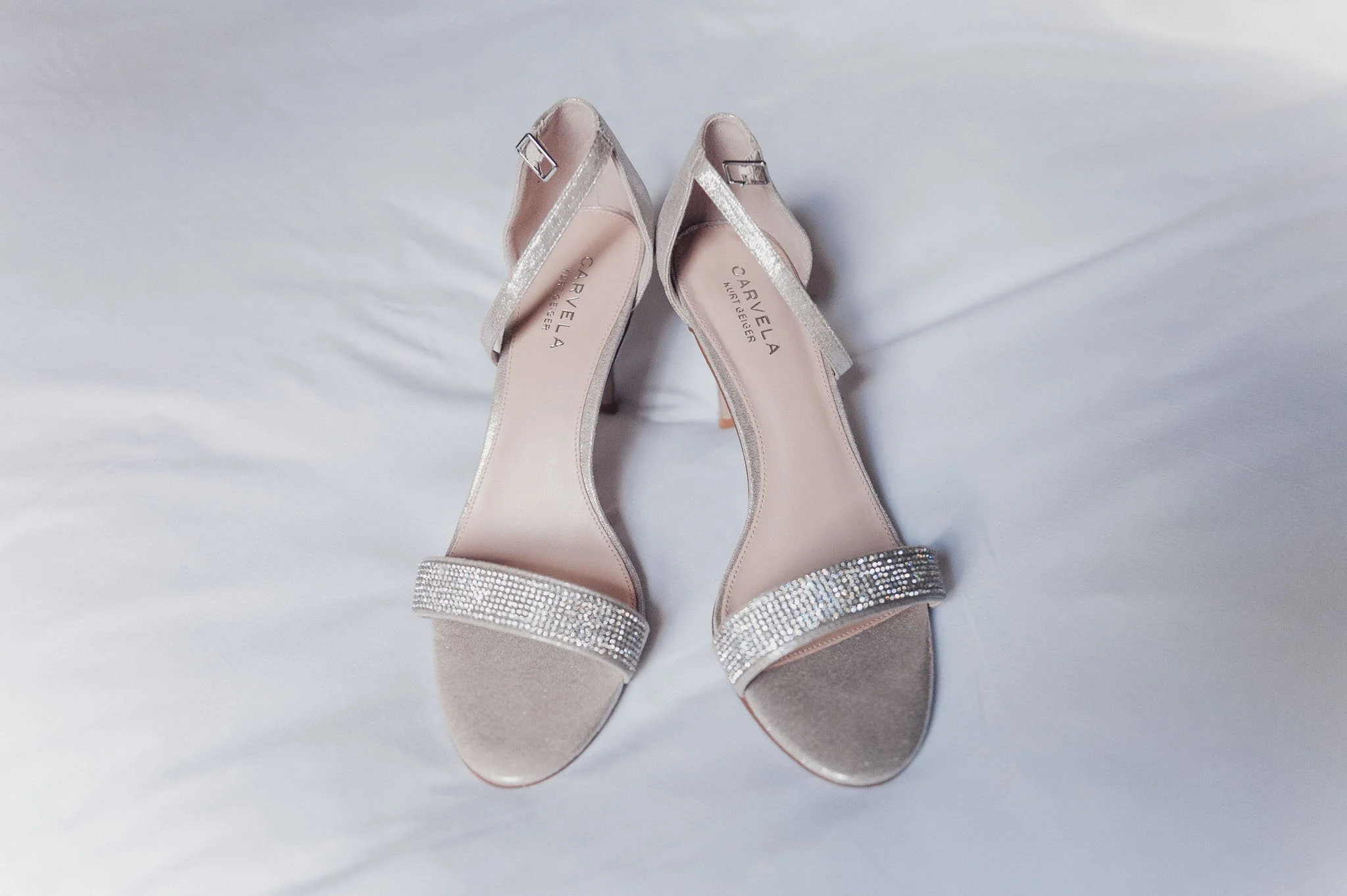 A pair of embellished bridal shoes laid out on a white bedspread.
