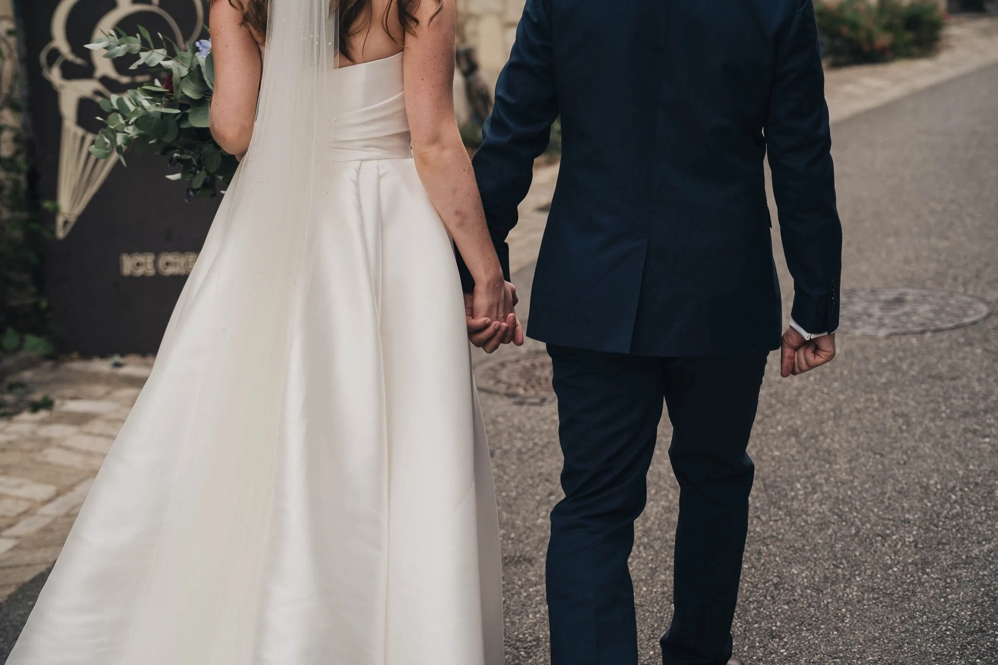 Bride and groom walking hand-in-hand down a village street in Aubeterre-sur-Dronne.