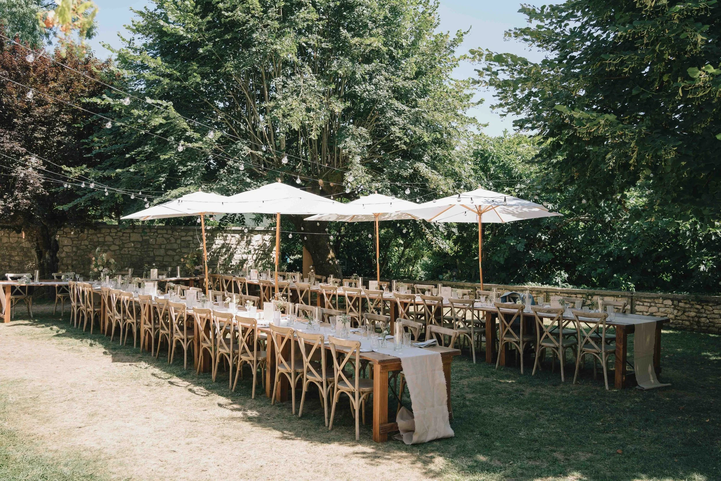 Outdoor wedding reception setup with long wooden tables, parasols, and string lights in southwest France
