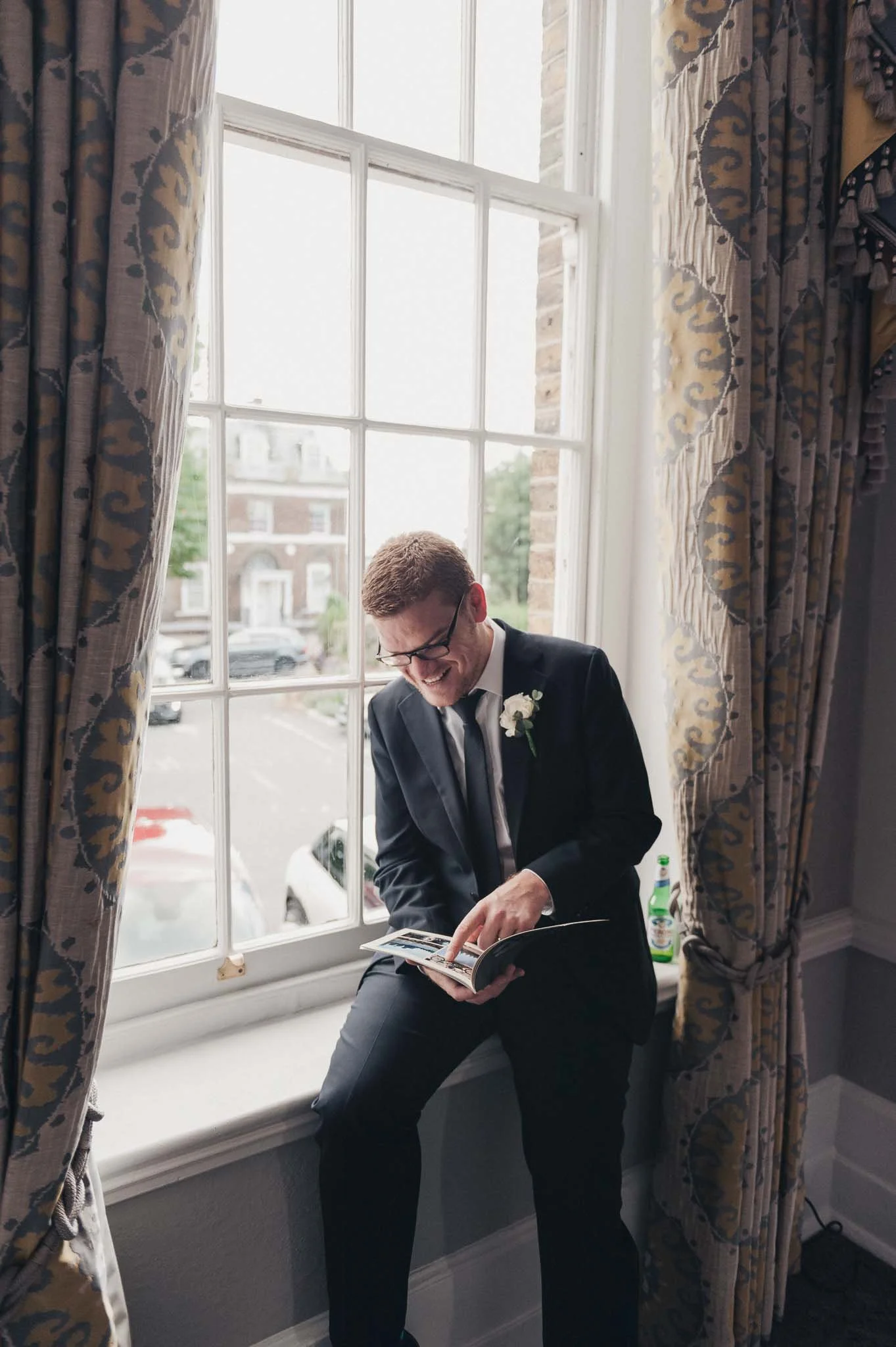 Groom sitting by the window reading a booklet during the reception at Richmond Hill Hotel.
