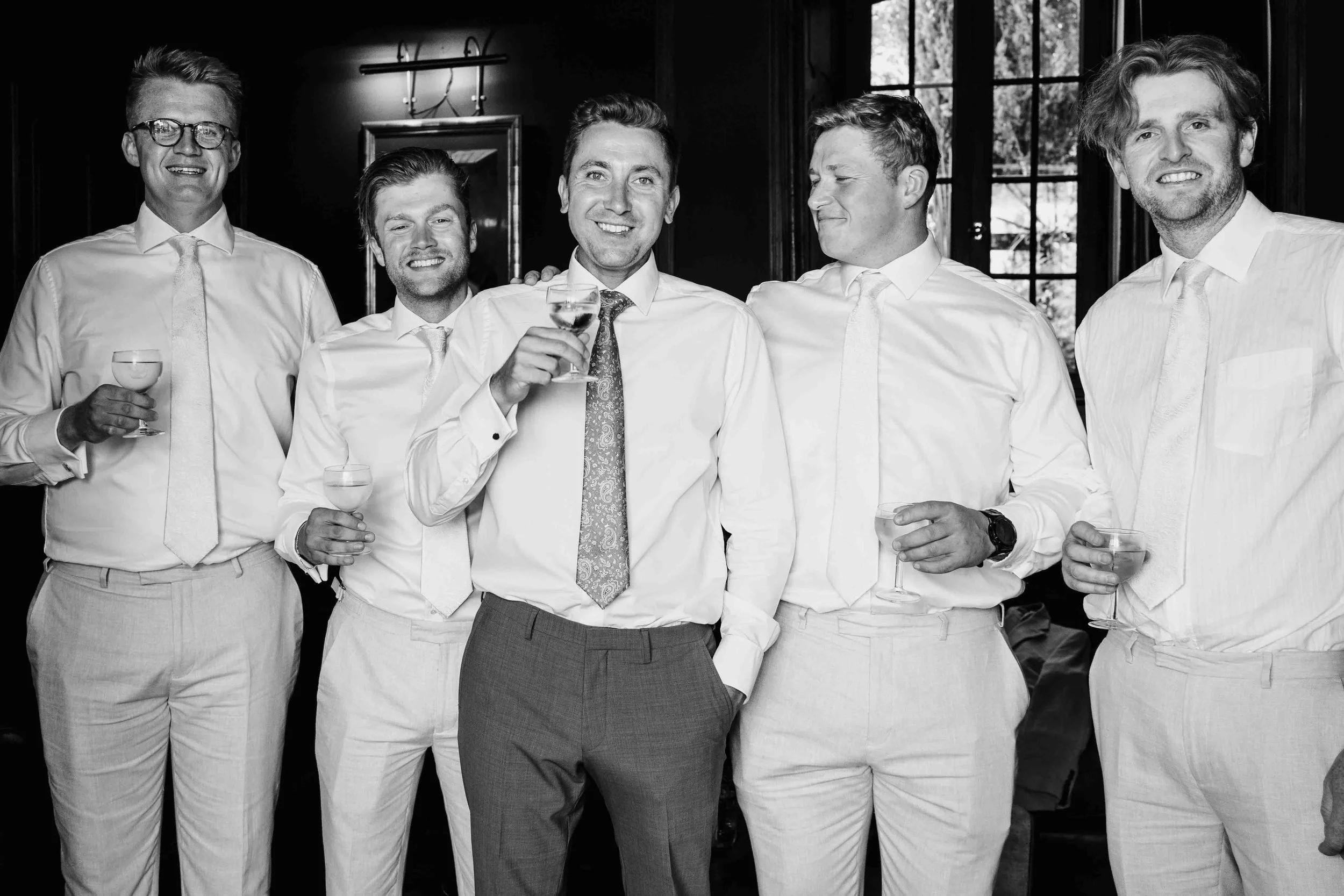 Group of groomsmen toasting with drinks in a relaxed black and white pre-ceremony moment