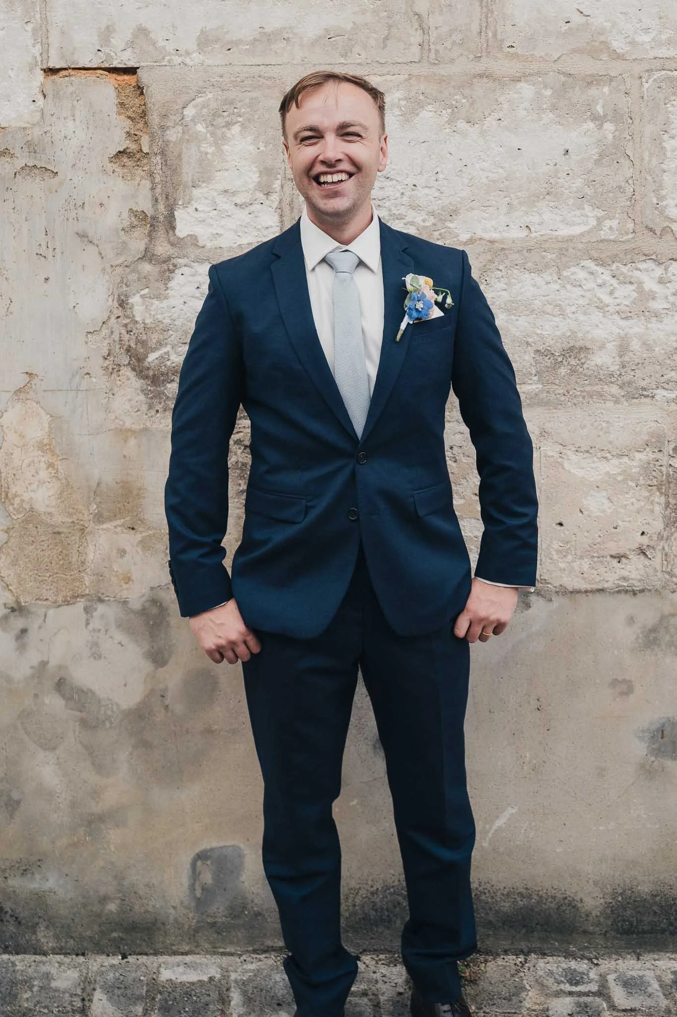 Groom standing for a portrait against a stone wall in Aubeterre-sur-Dronne.