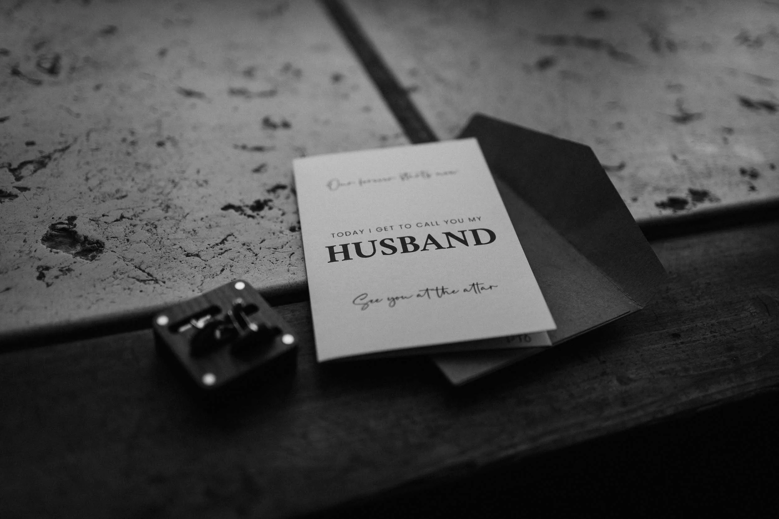Black and white detail of cufflinks and a "Husband" card on the wedding morning
