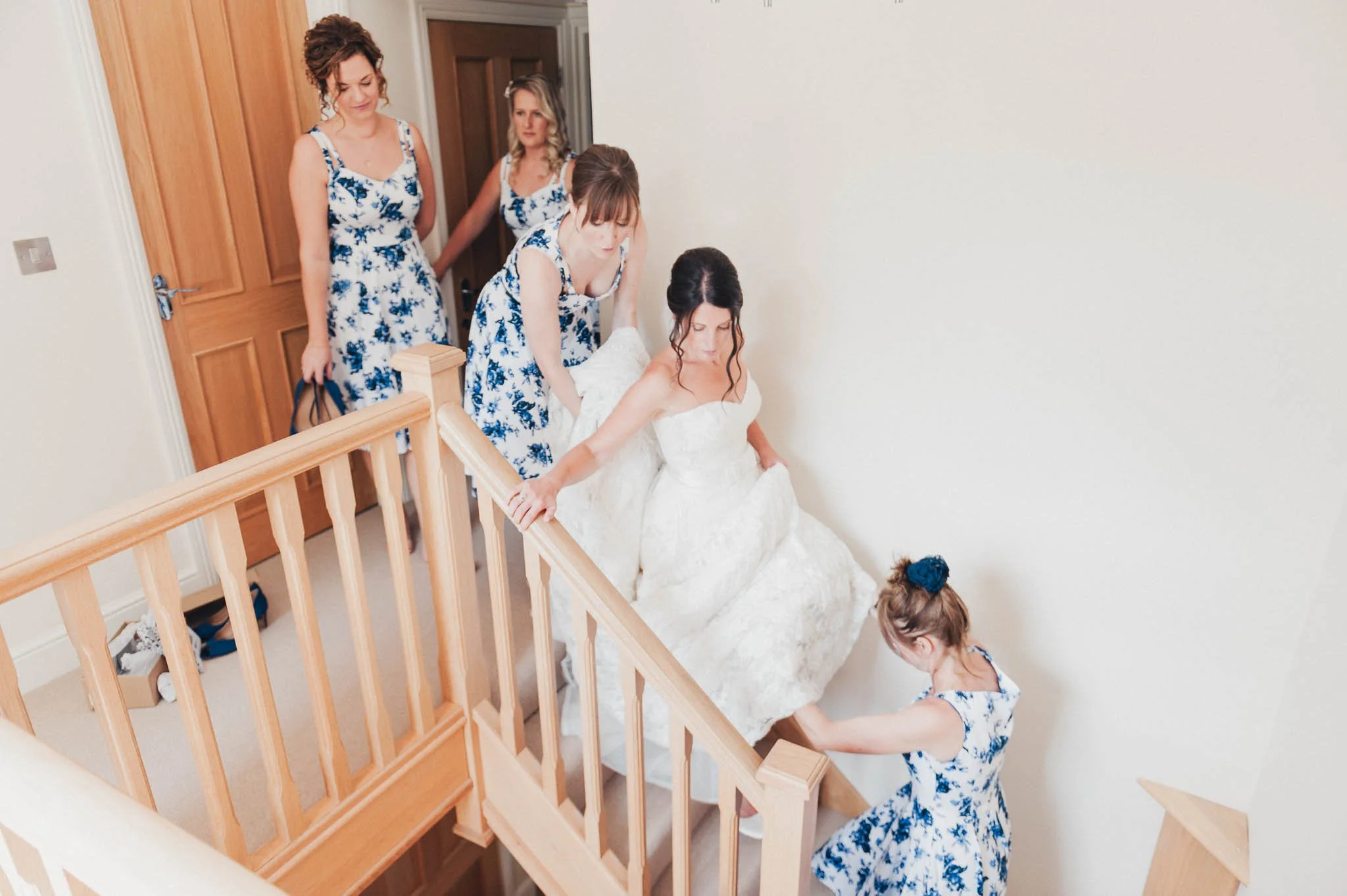 The bride walking downstairs with help from bridesmaids lifting her dress.