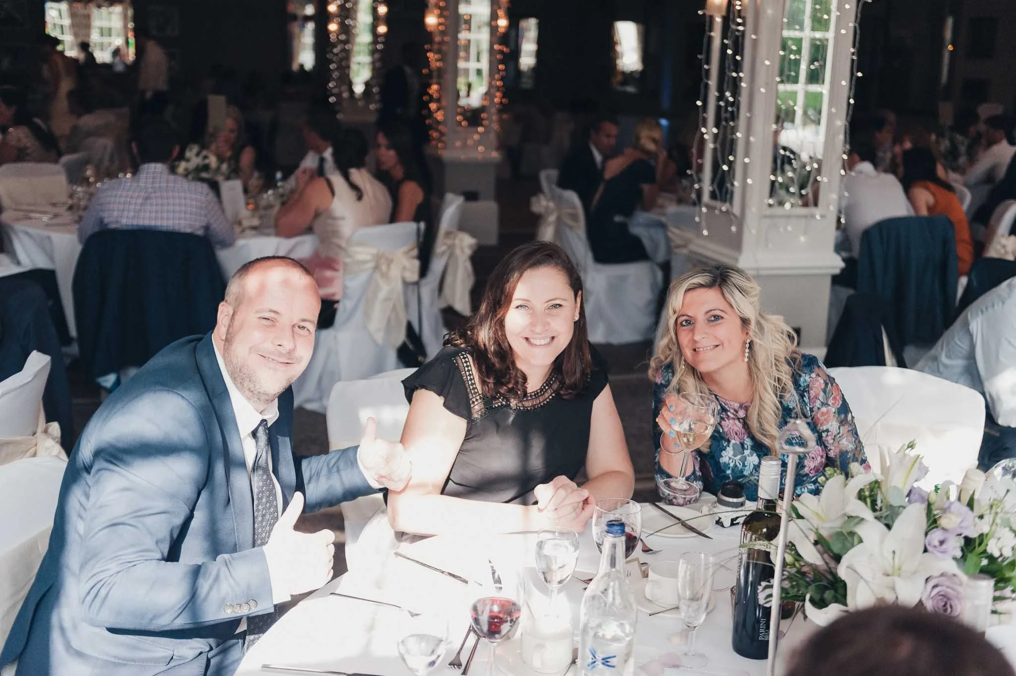 Three guests smiling for a photo at their table during the wedding reception.
