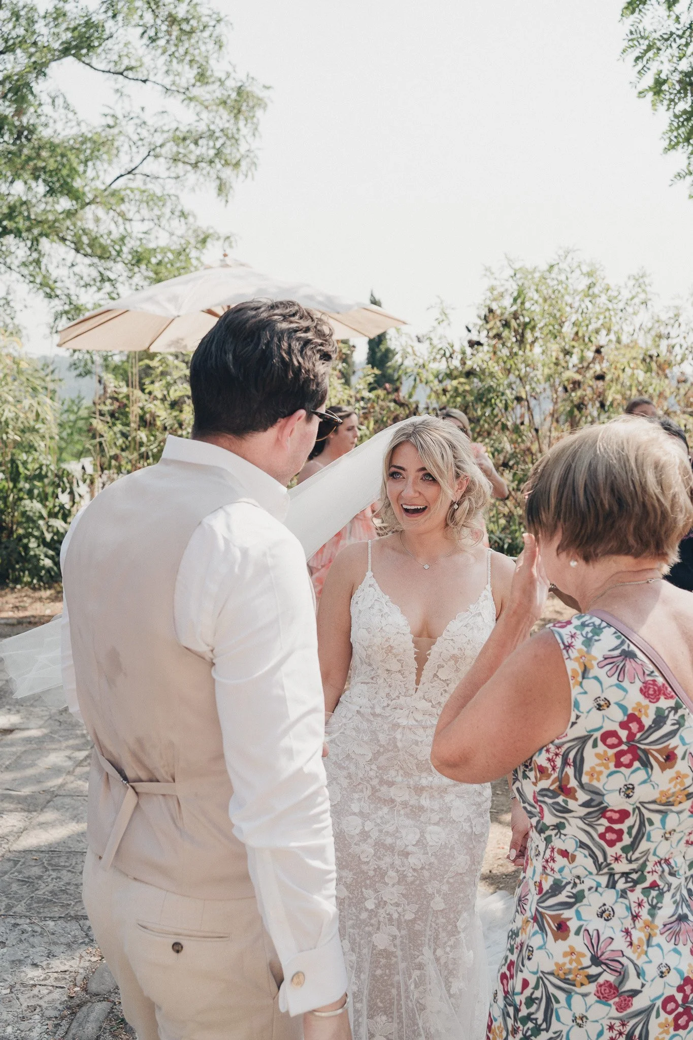 Bride laughing with the groom and a guest during the outdoor reception.
