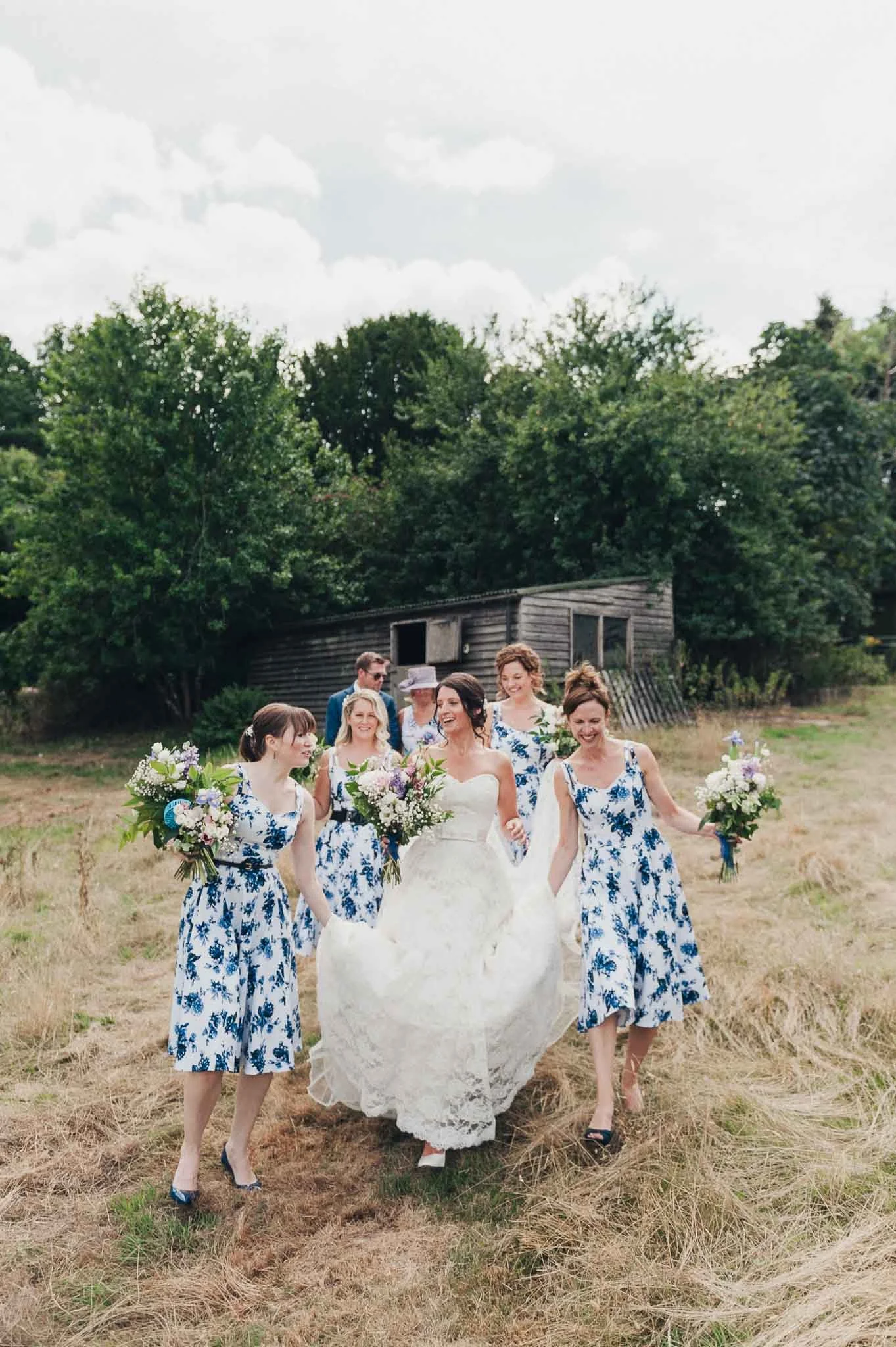 The bride and bridesmaids walking together through a field carrying bouquets.