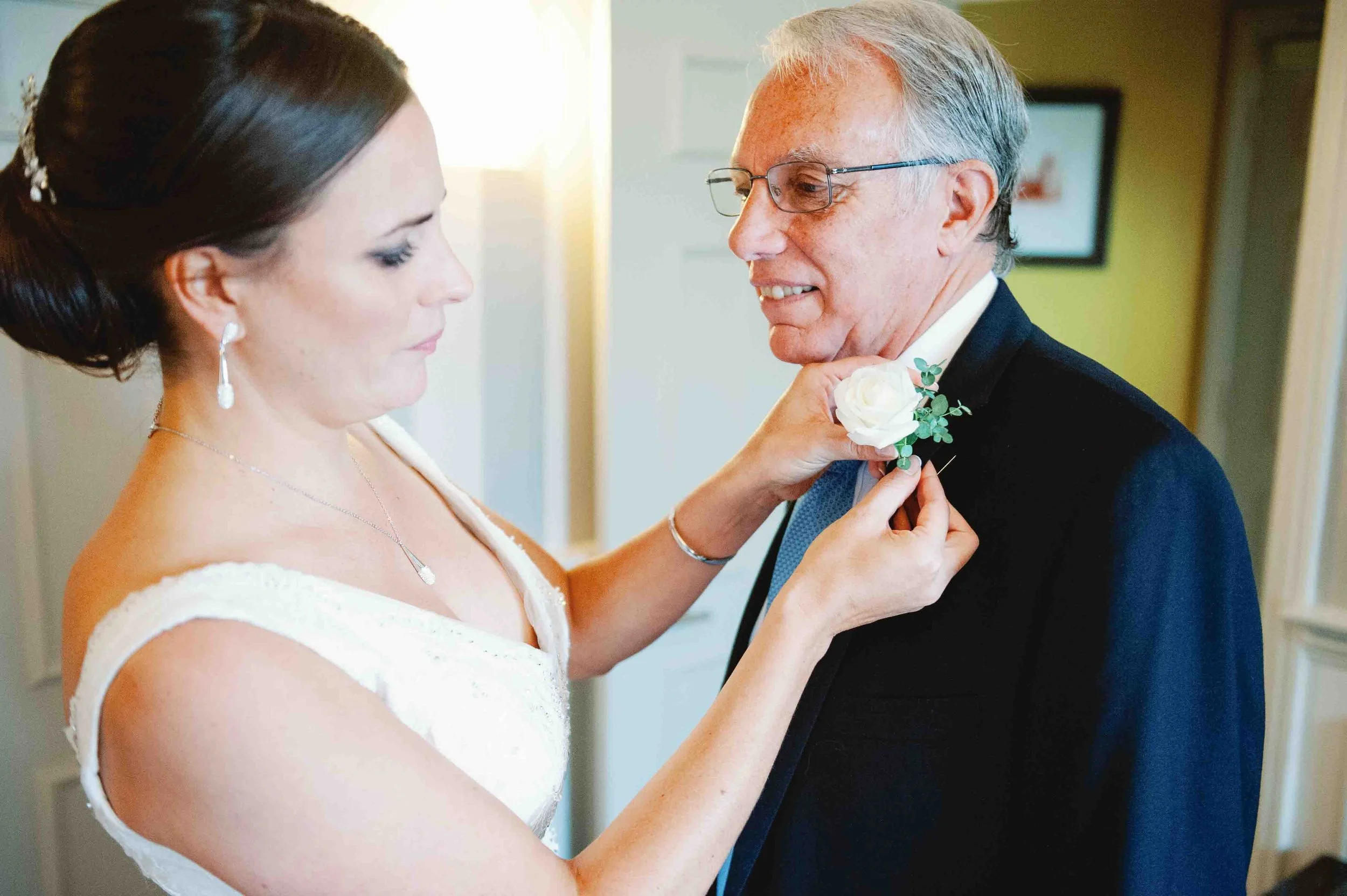 Bride quietly helps her father adjust his boutonnière before the ceremony, a calm and intimate moment during a wedding morning in France.