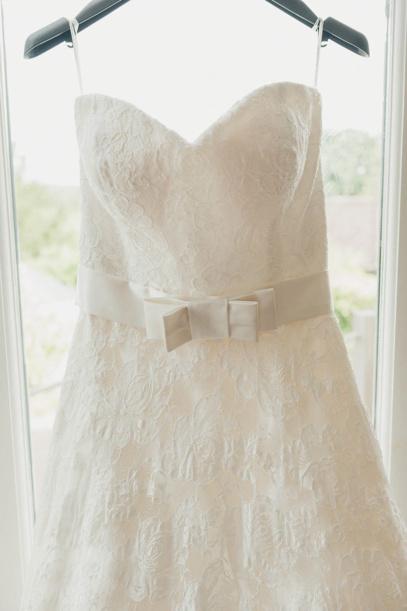 The bride’s lace wedding dress hanging in a bright doorway before the ceremony.