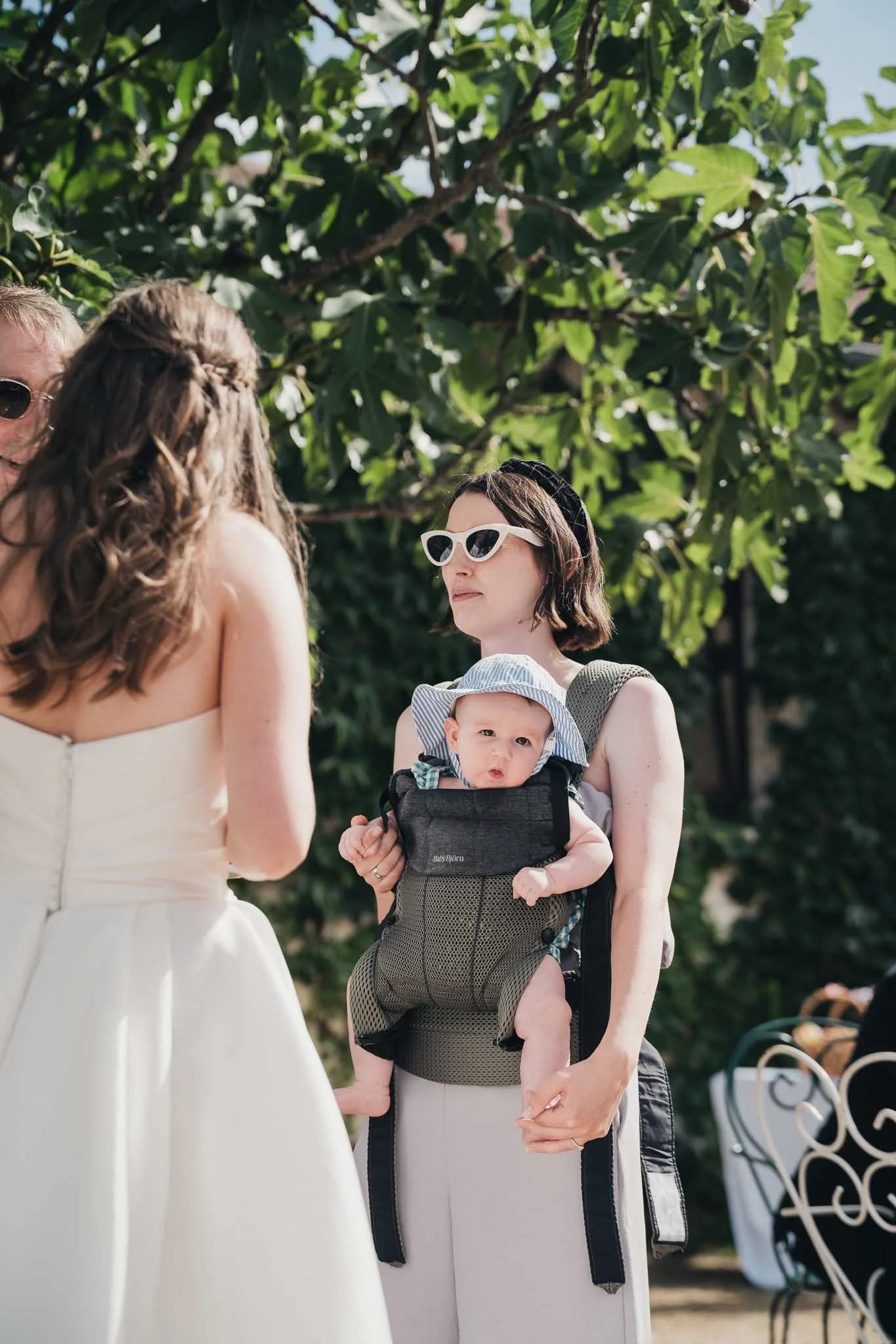 Guest holding a baby in the shade during the drinks reception at Manoir de Longeveau.