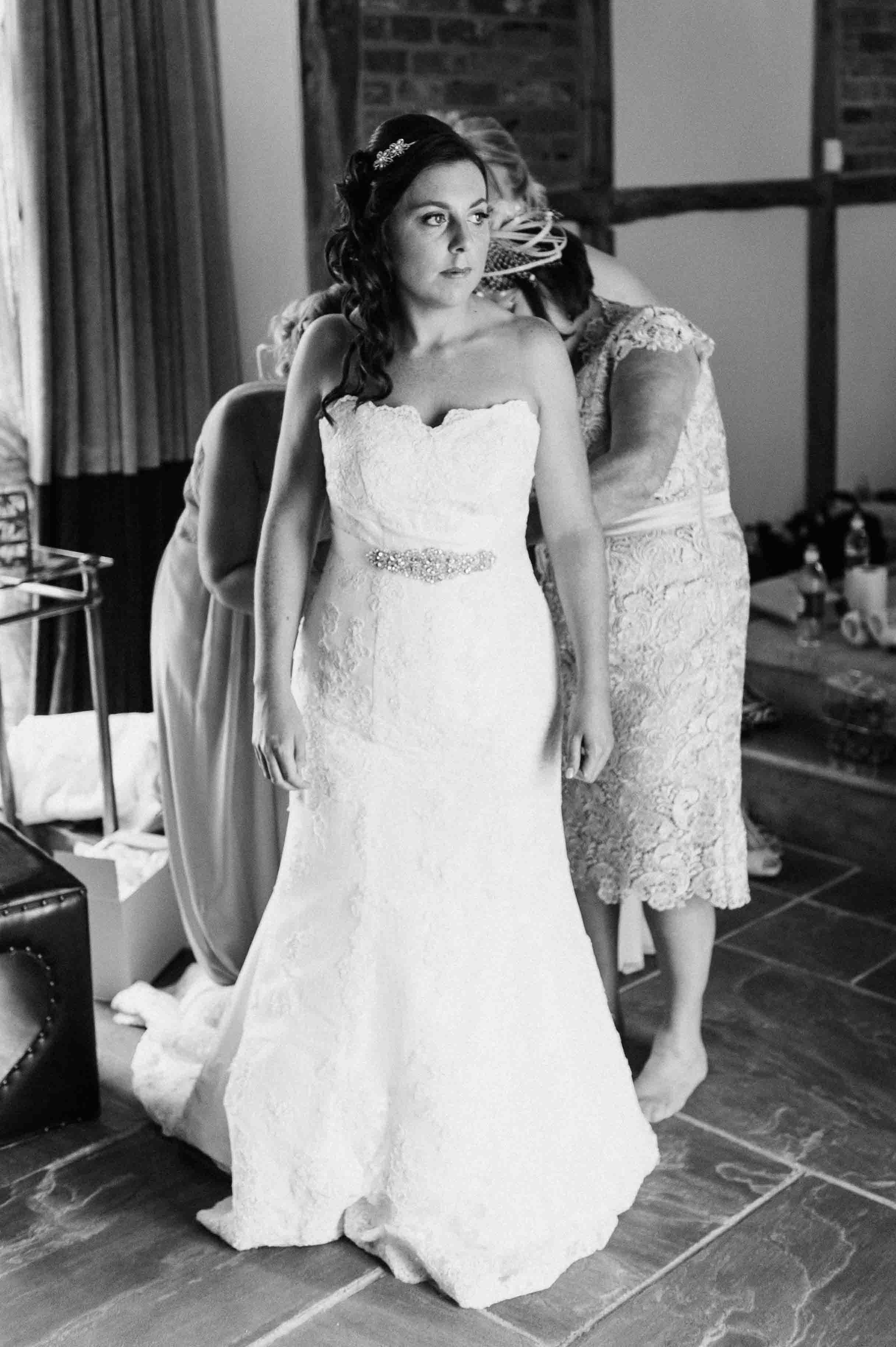 Bride being helped into her wedding dress by a family member during a quiet getting-ready moment, photographed in a natural, documentary style.