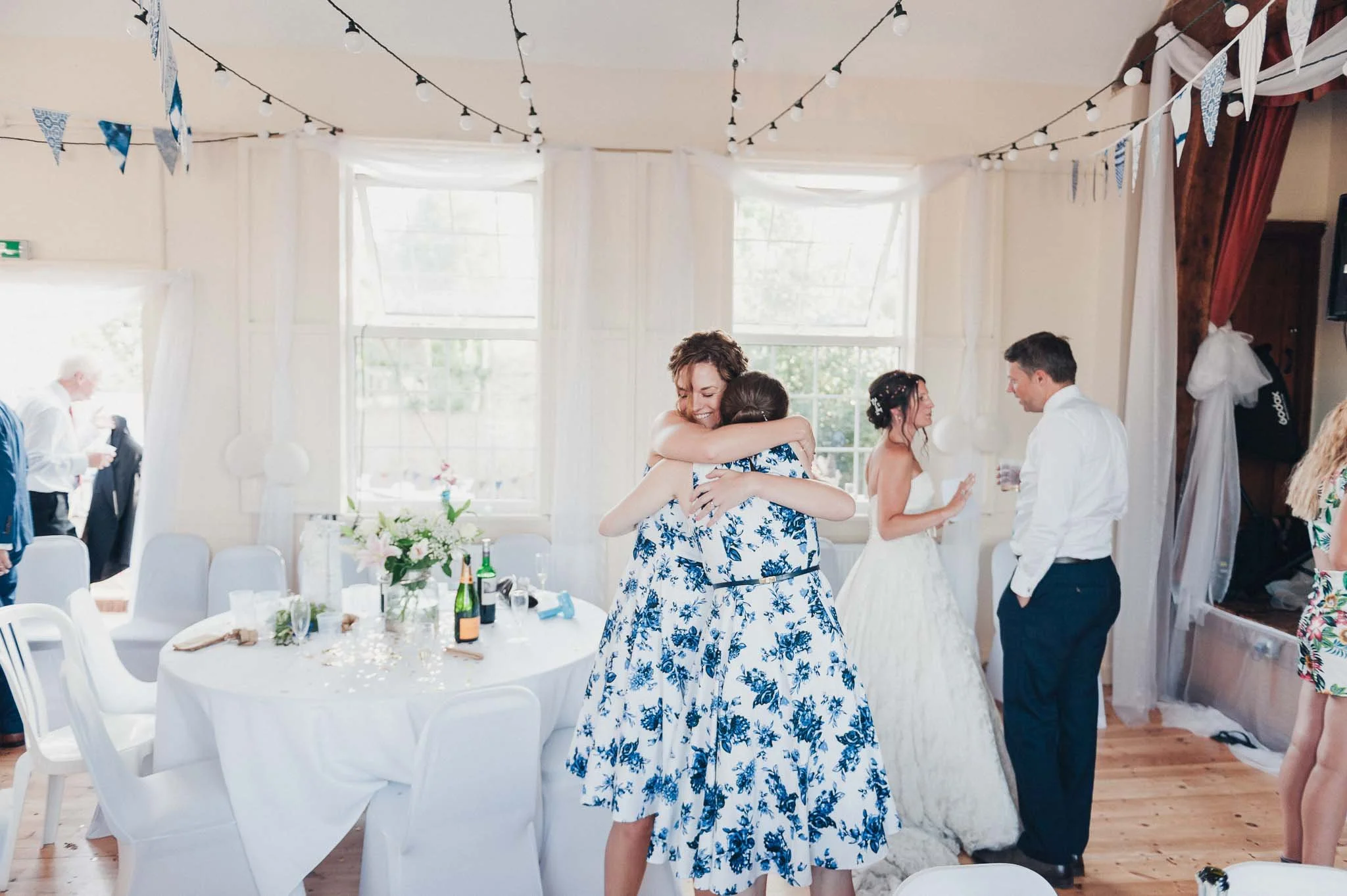 The bride hugging a bridesmaid during the reception inside the village hall.