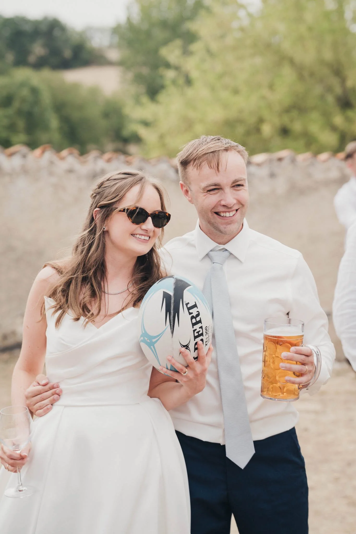 Bride and groom posing with the rugby ball and a beer, smiling during the celebrations.