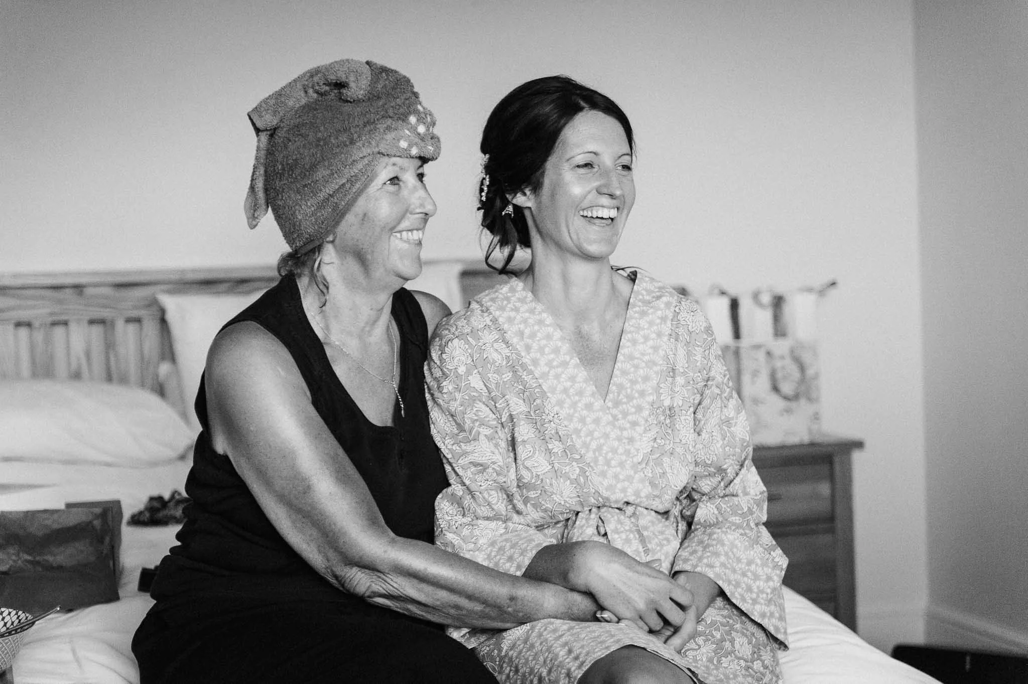 The bride and her mum sitting on the bed, laughing together during morning preparations.