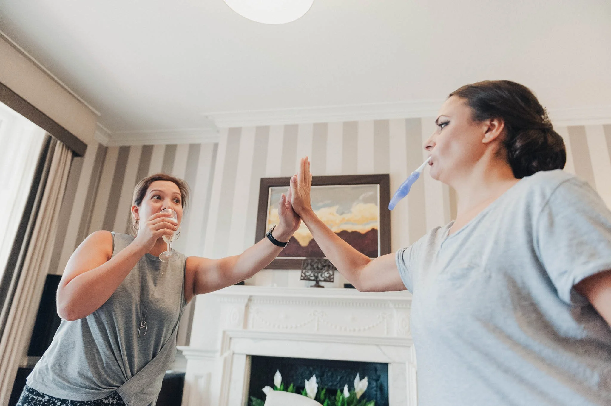 Bridesmaid giving the bride a playful high-five during morning preparations.
