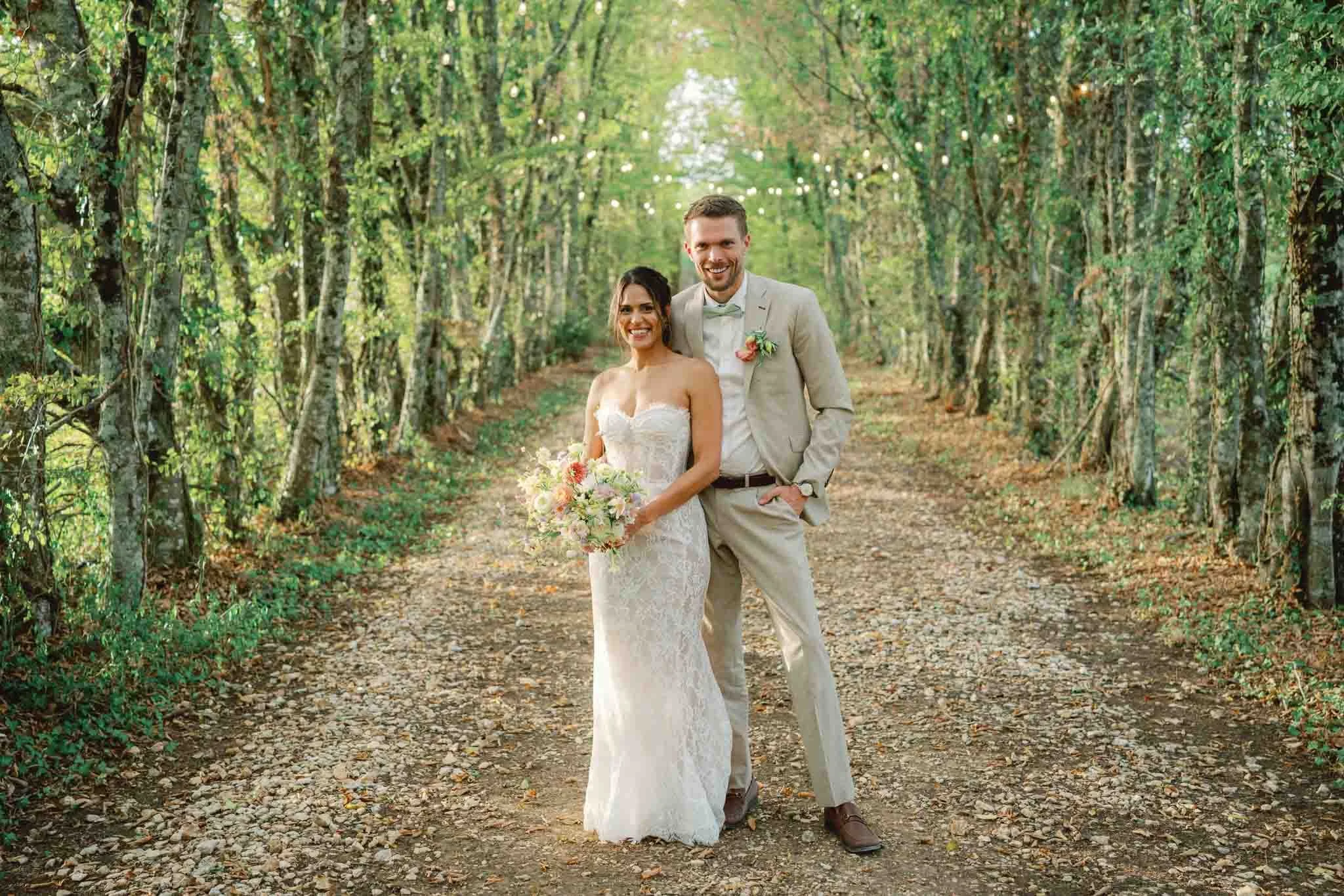 Bride and groom smiling together on a tree-lined path with fairy lights, Bordeaux wedding photography