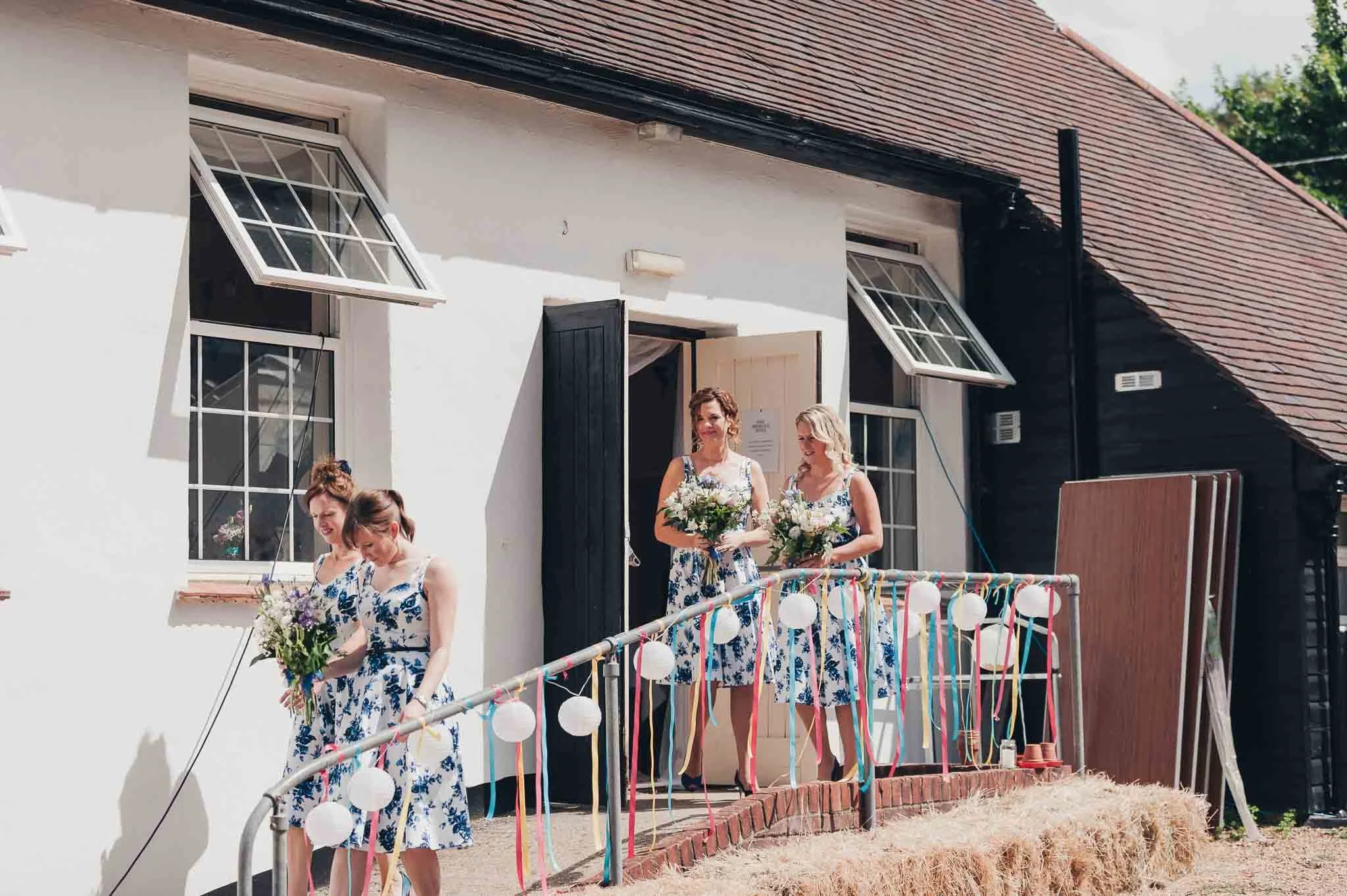 Bridesmaids standing outside the village hall holding their bouquets before walking to the ceremony.