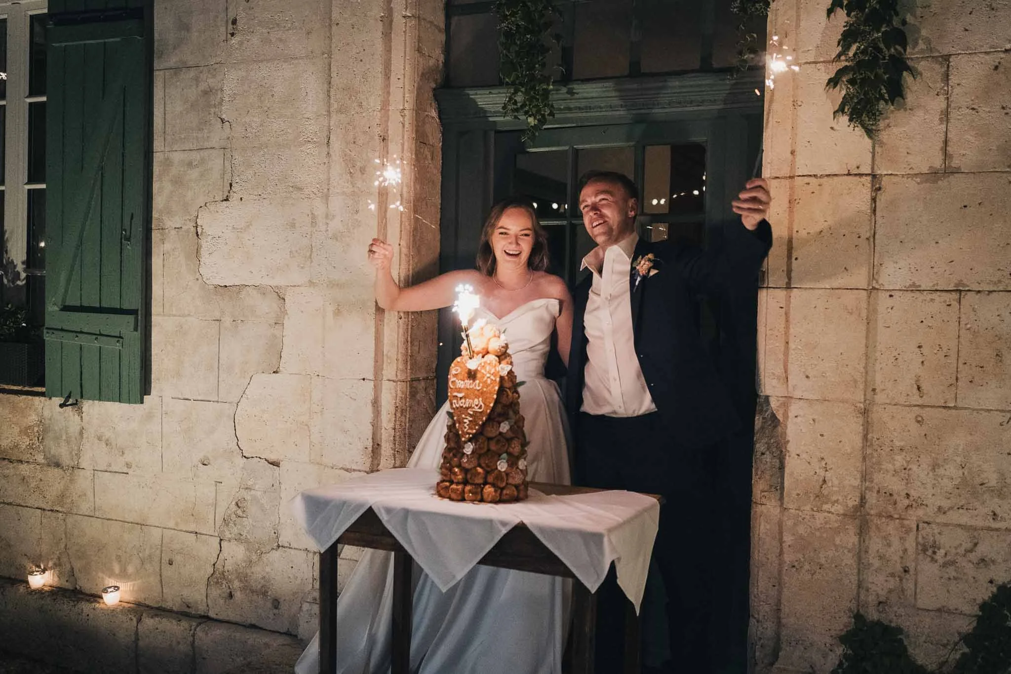 Bride and groom standing with their croquembouche wedding cake, sparklers lit on top.