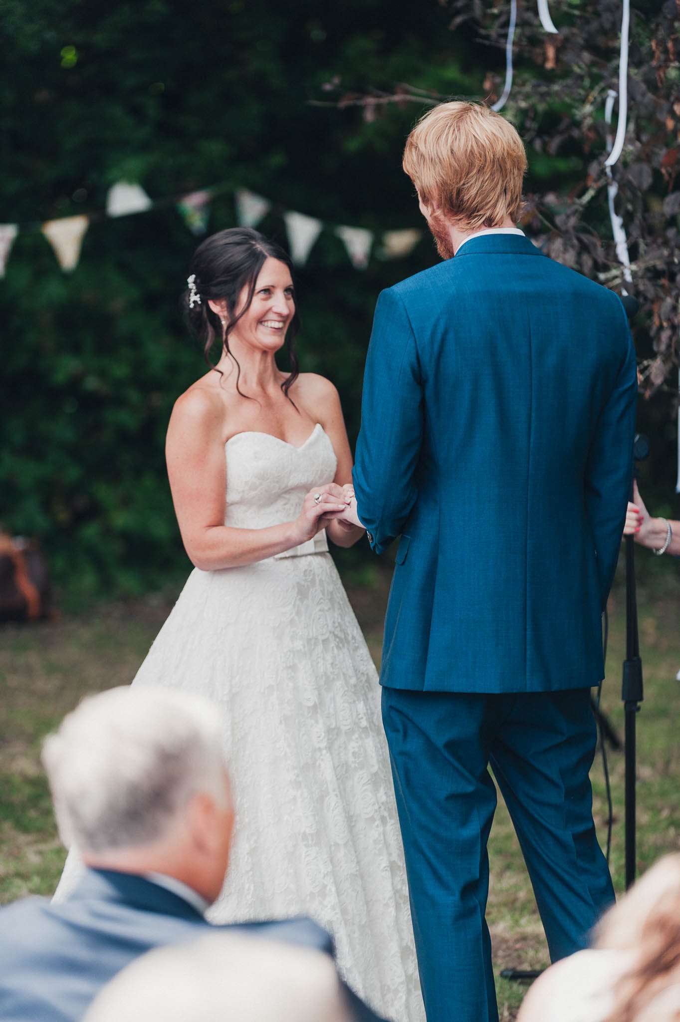 Wide shot of the bride and groom standing under bunting during the outdoor ceremony.