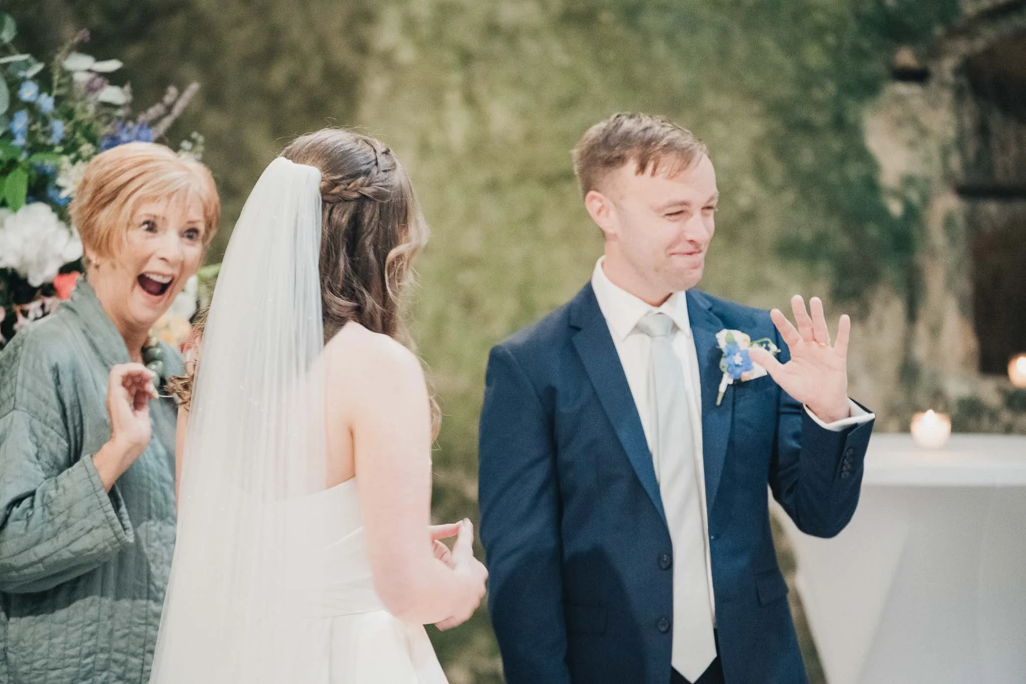 Bride and groom smiling during the vows, with a guest reacting behind them inside the Église Souterraine Saint-Jean.