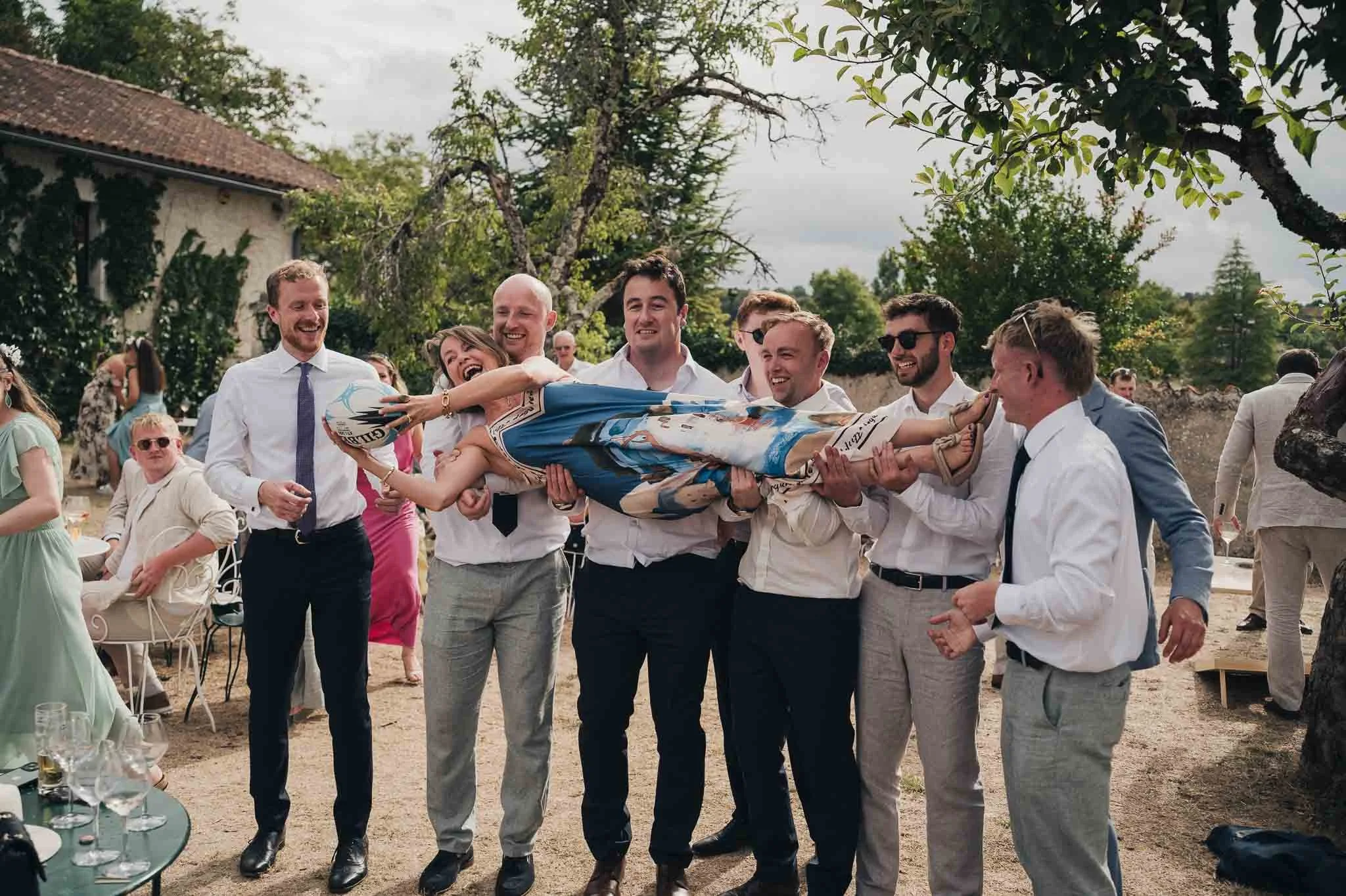 Group of guests holding up Grooms Mother while laughing during the afternoon reception.
