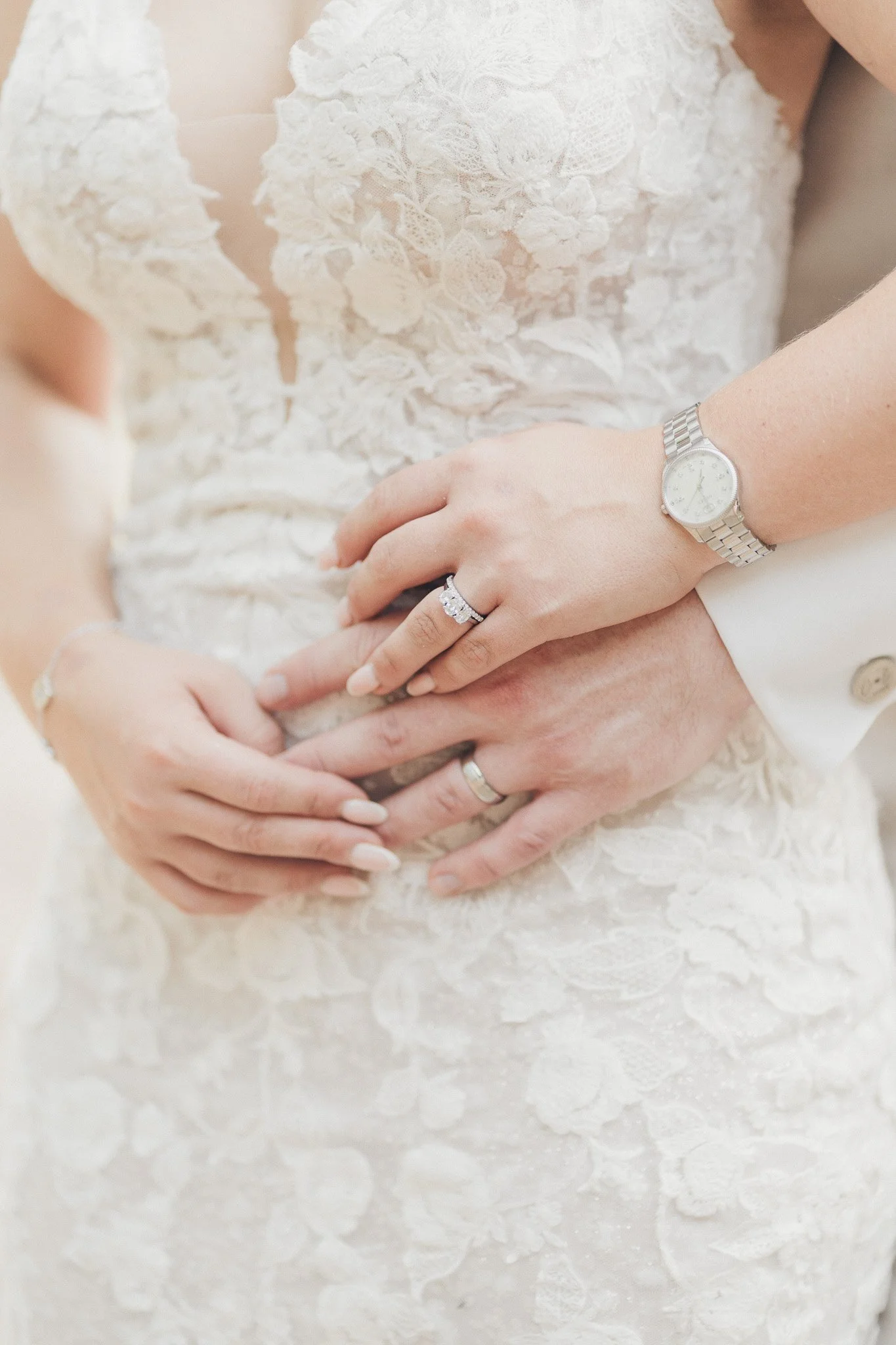 Close-up of the bride’s hands resting on her wedding dress, showing rings and lace detail.