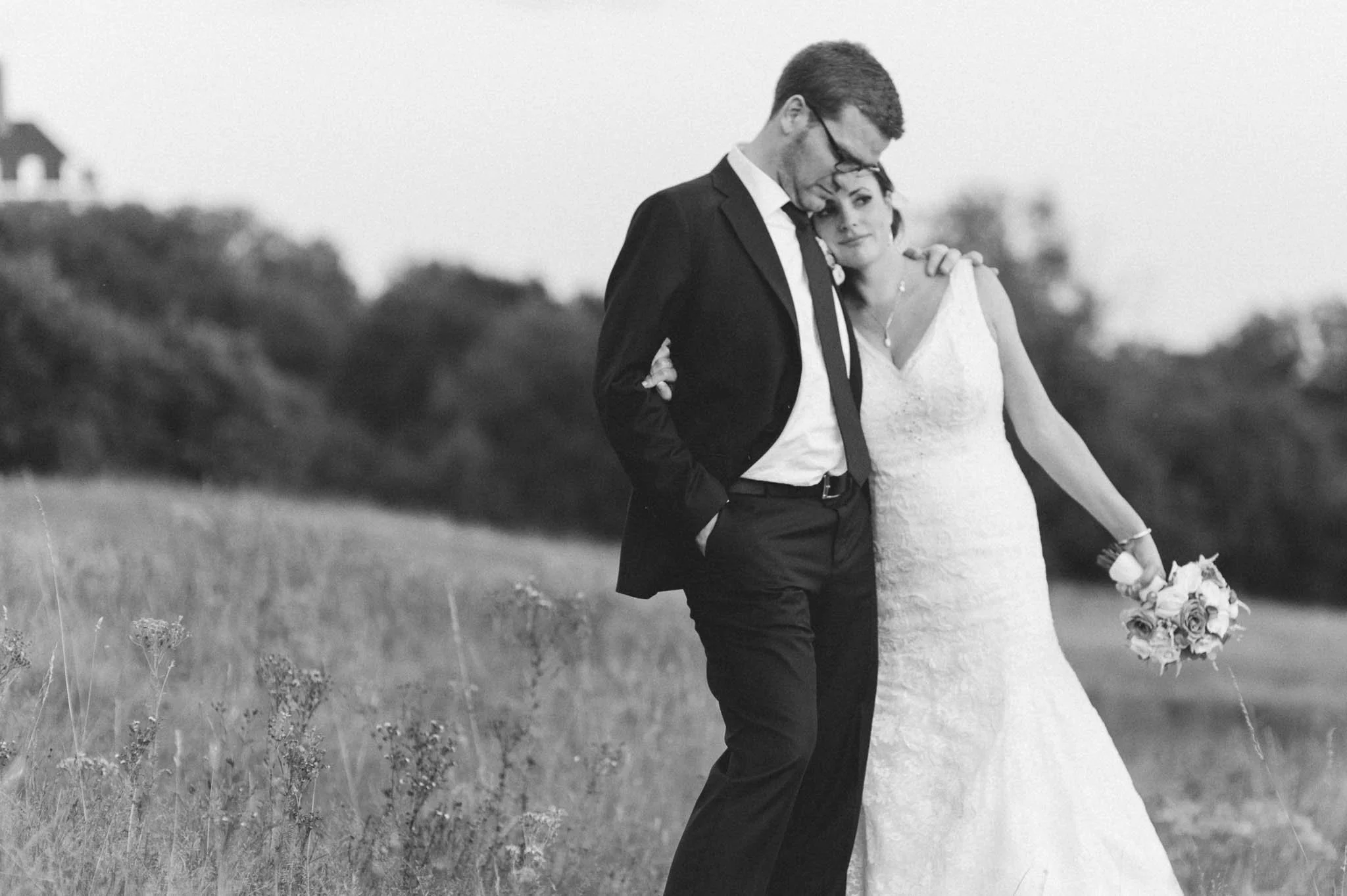 Black and white photograph of bride and groom walking through a field
