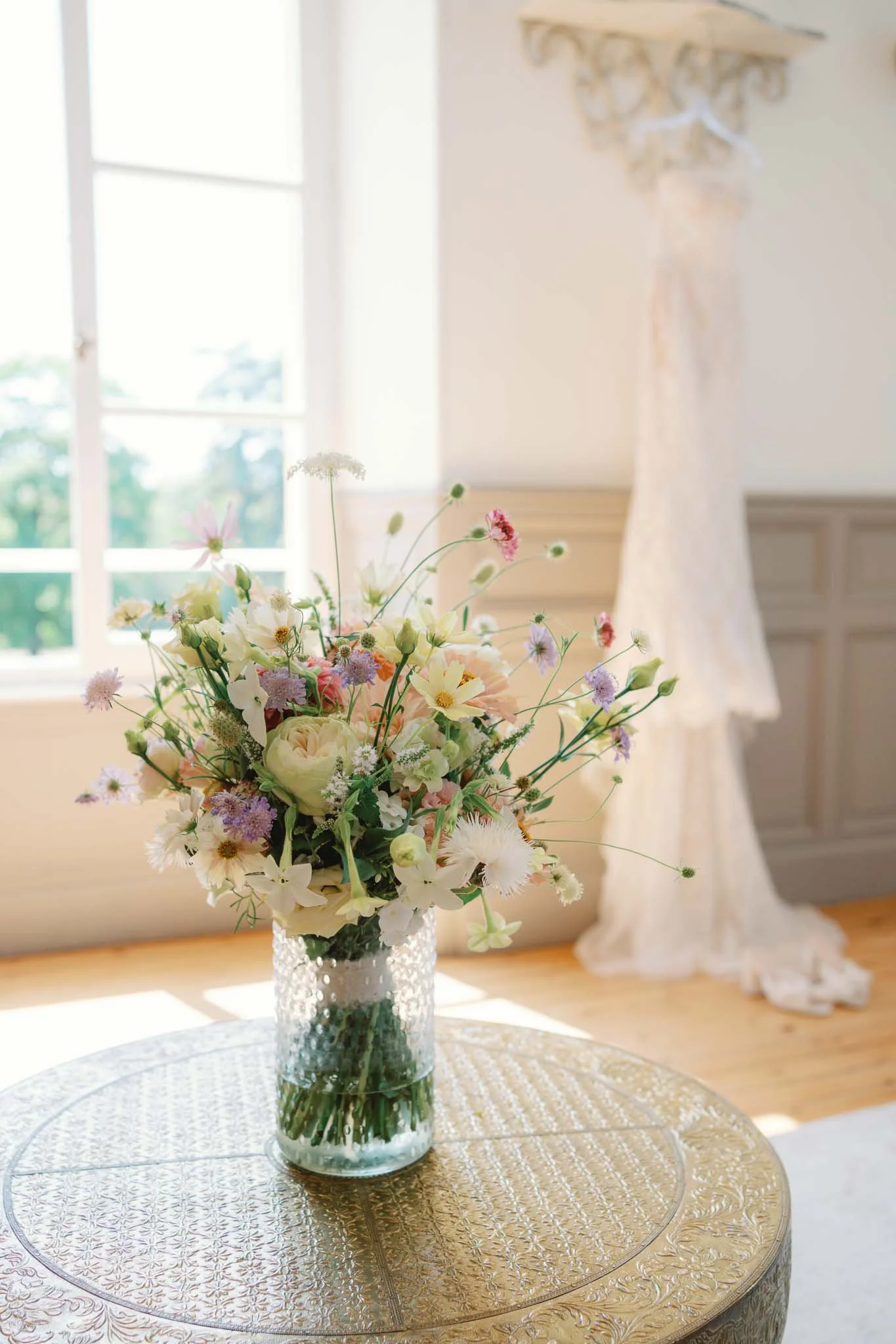 Bridal bouquet in a vase with the wedding dress in the background at Château de Sainte Croix, Dordogne