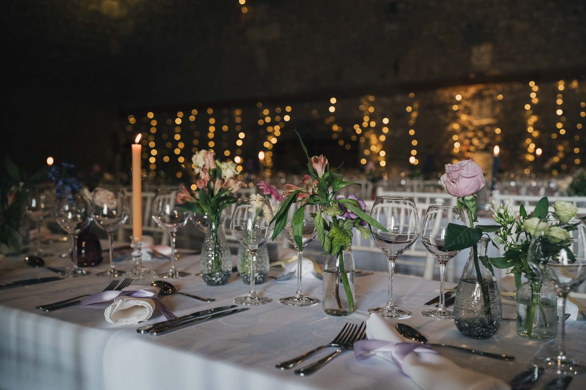 Close-up of the wedding dinner table with glassware, candles and floral arrangements.