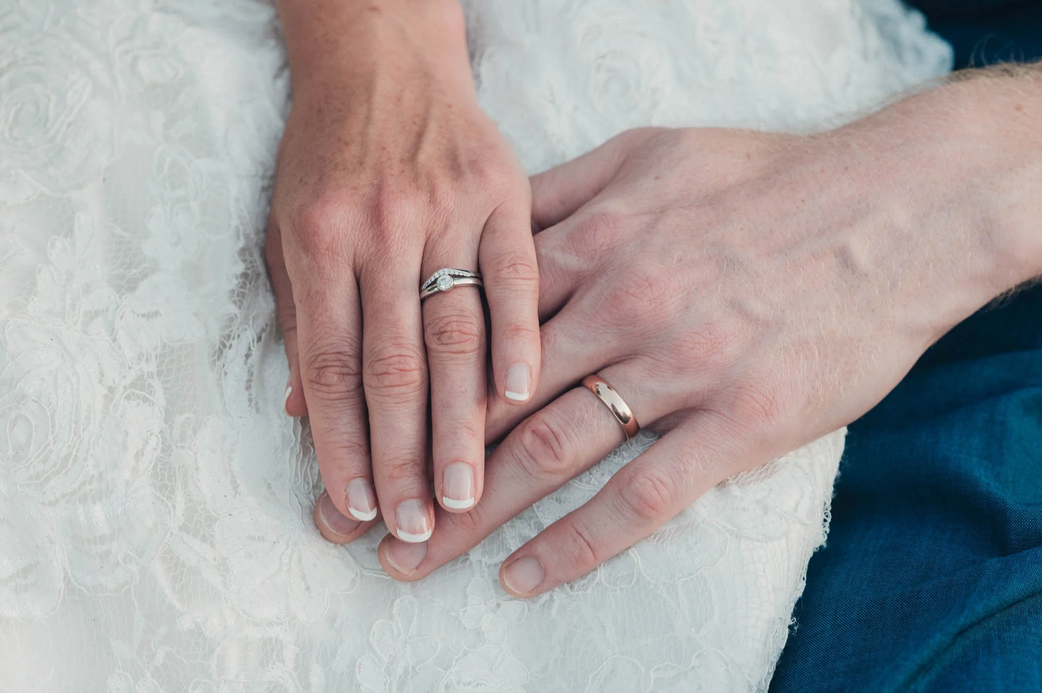 Close-up of the bride and groom’s hands resting together, showing their wedding rings.
