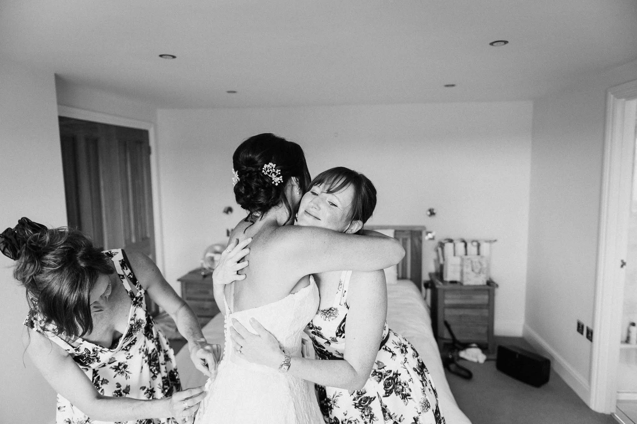 Bridesmaids helping one another get ready, hugged and laughing together.