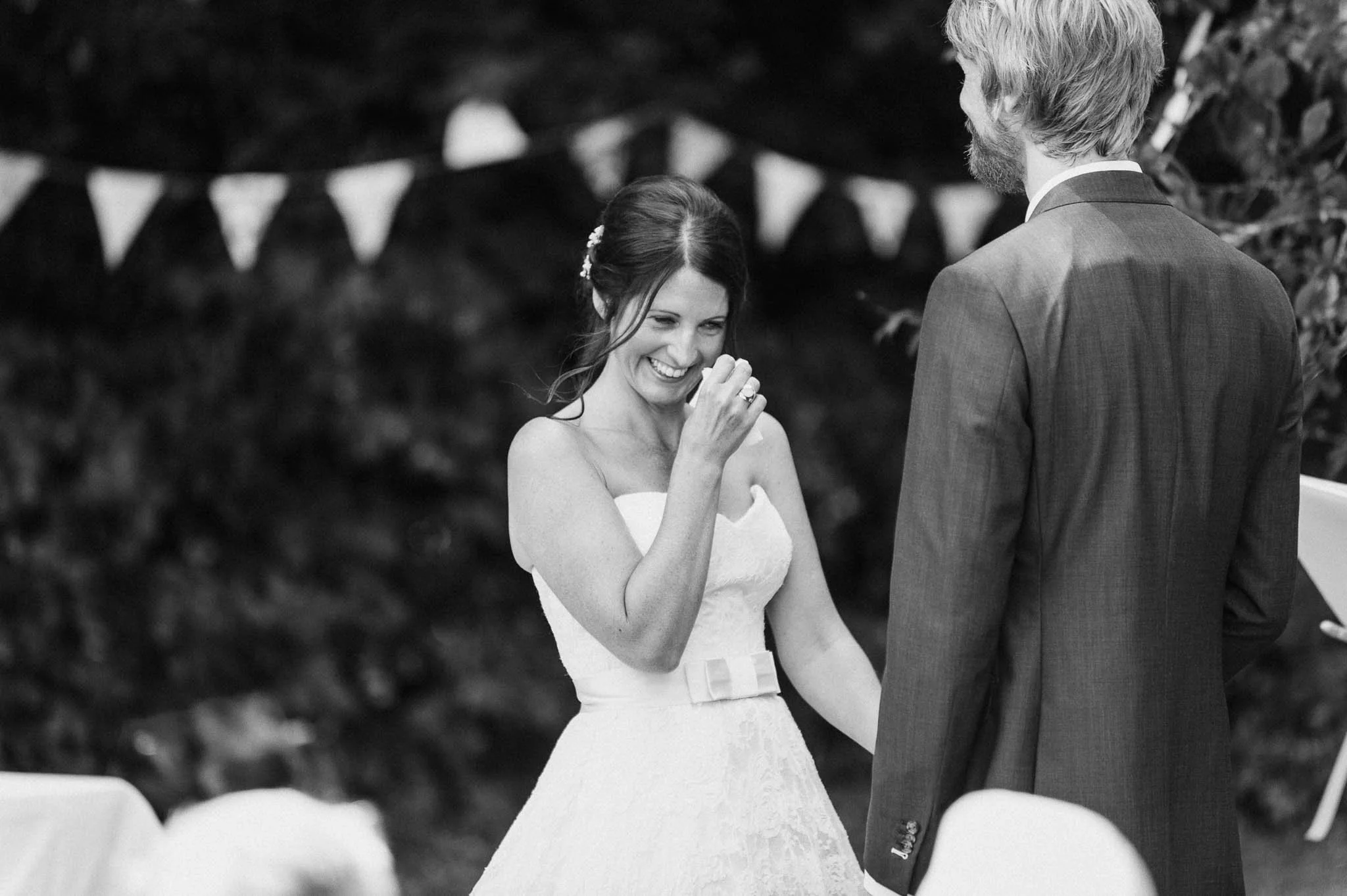 Black-and-white photo of the bride laughing as she reads her vows to the groom.