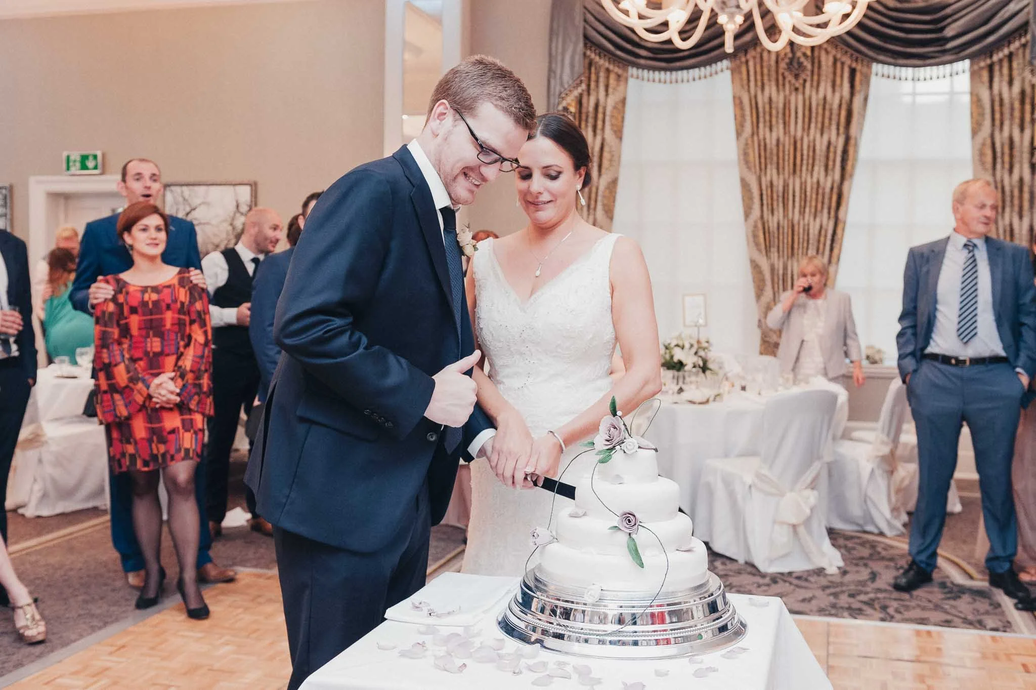 The bride and groom cutting their tiered wedding cake together at the reception.