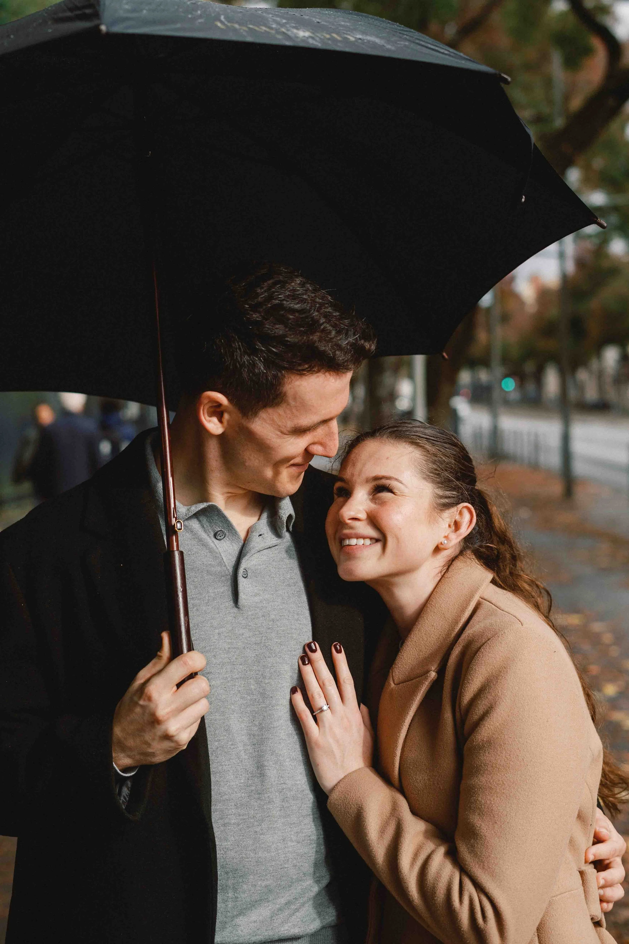Newly engaged couple sharing an umbrella on a rainy day in Bordeaux