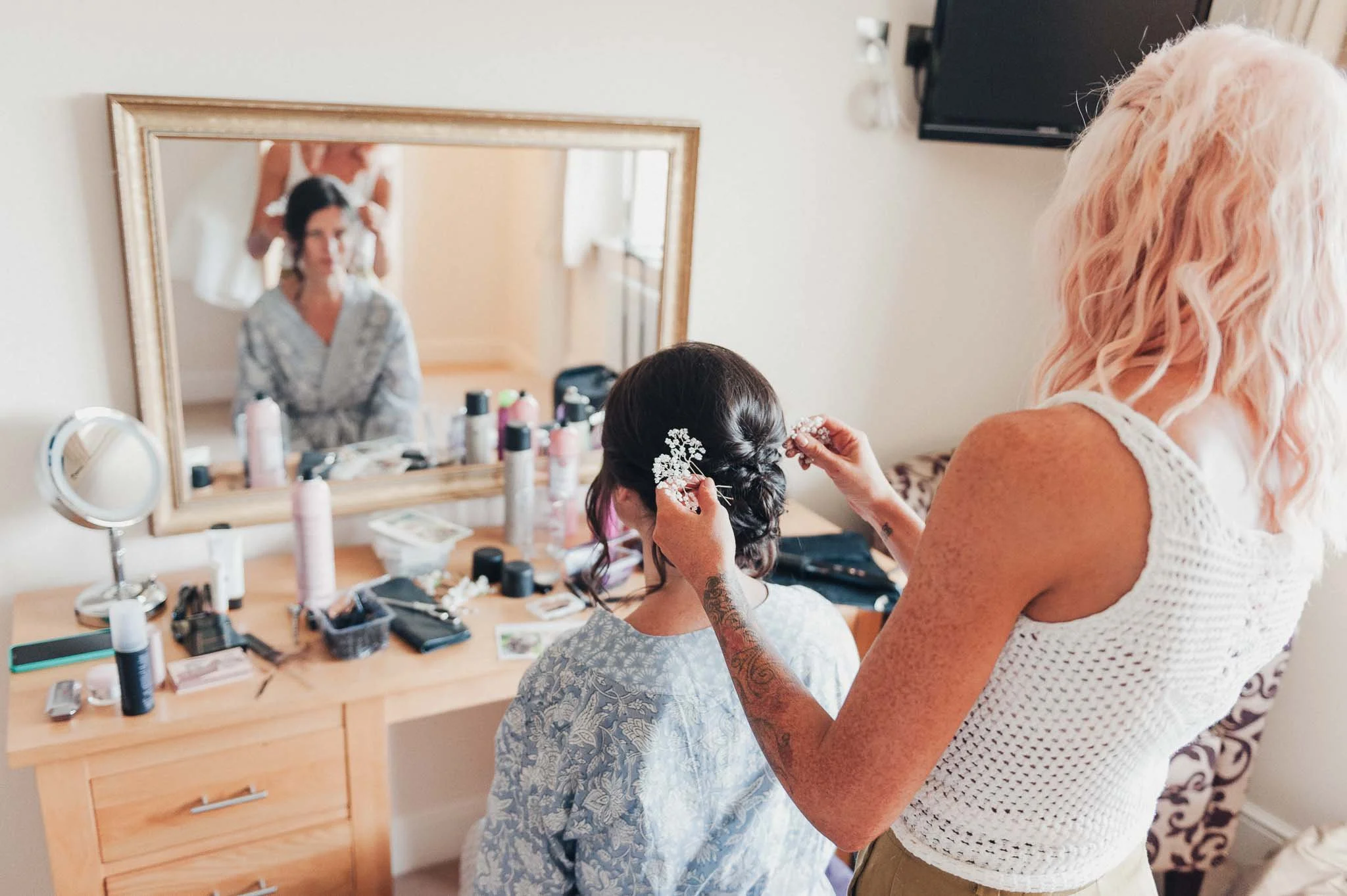 The bride having her makeup done in a bright bedroom while bridesmaids get ready around her.