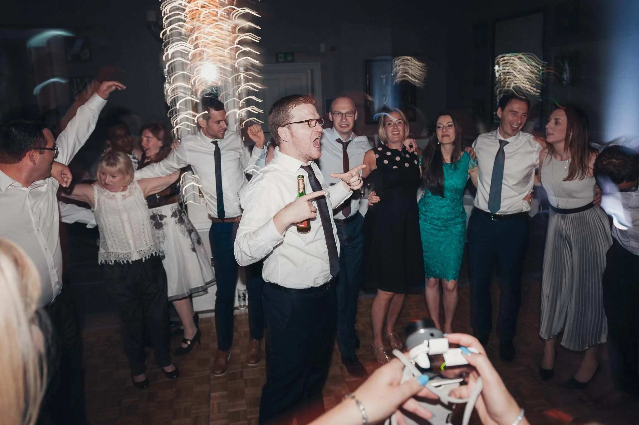 Guests cheering and dancing together on the wedding reception dance floor.