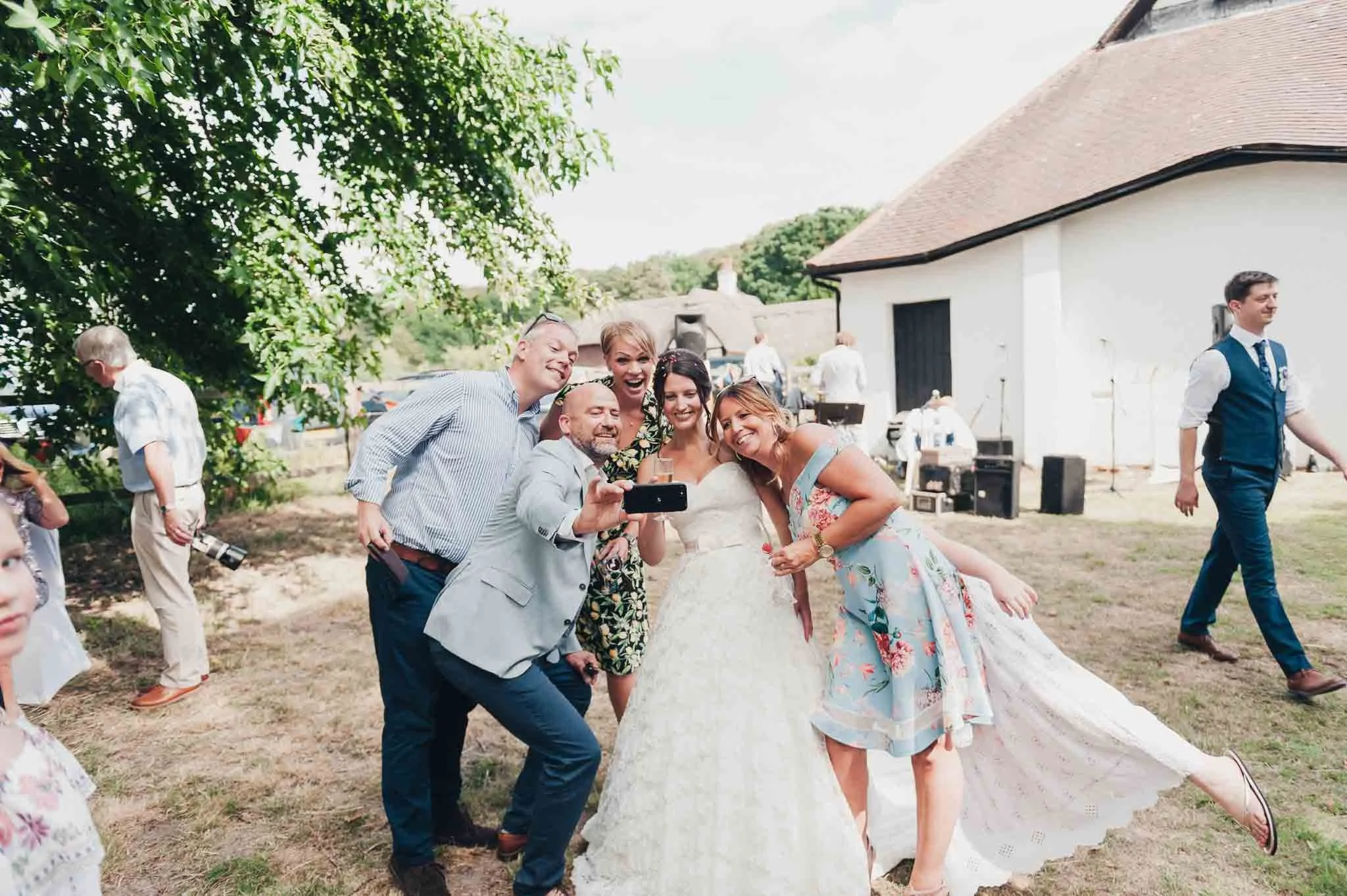 The bride surrounded by guests celebrating and laughing during group photos.